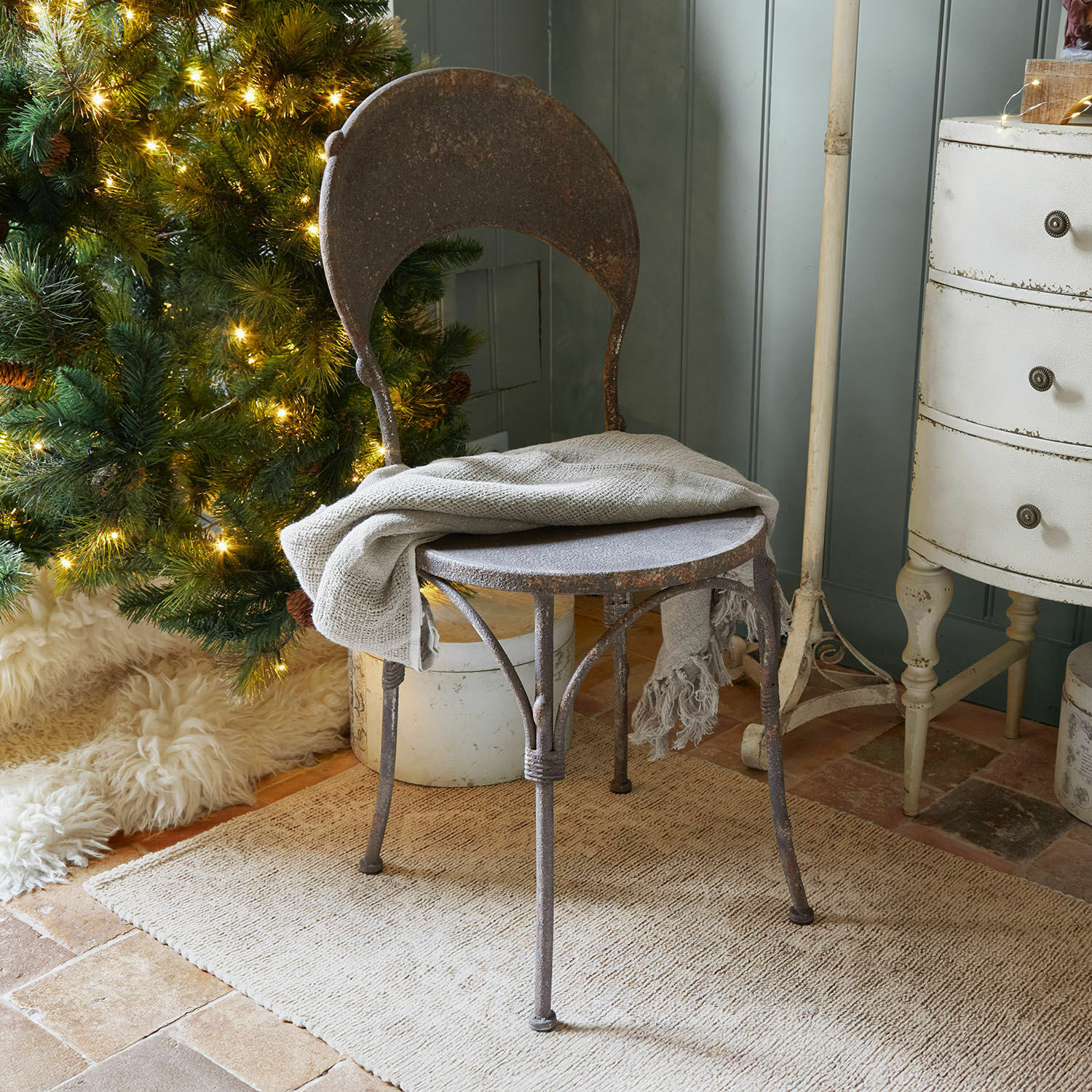 Stuhl Delivora Rustikaler Metallstuhl mit Rostpatina und grauem Plaid vor beleuchtetem Weihnachtsbaum und Teppich