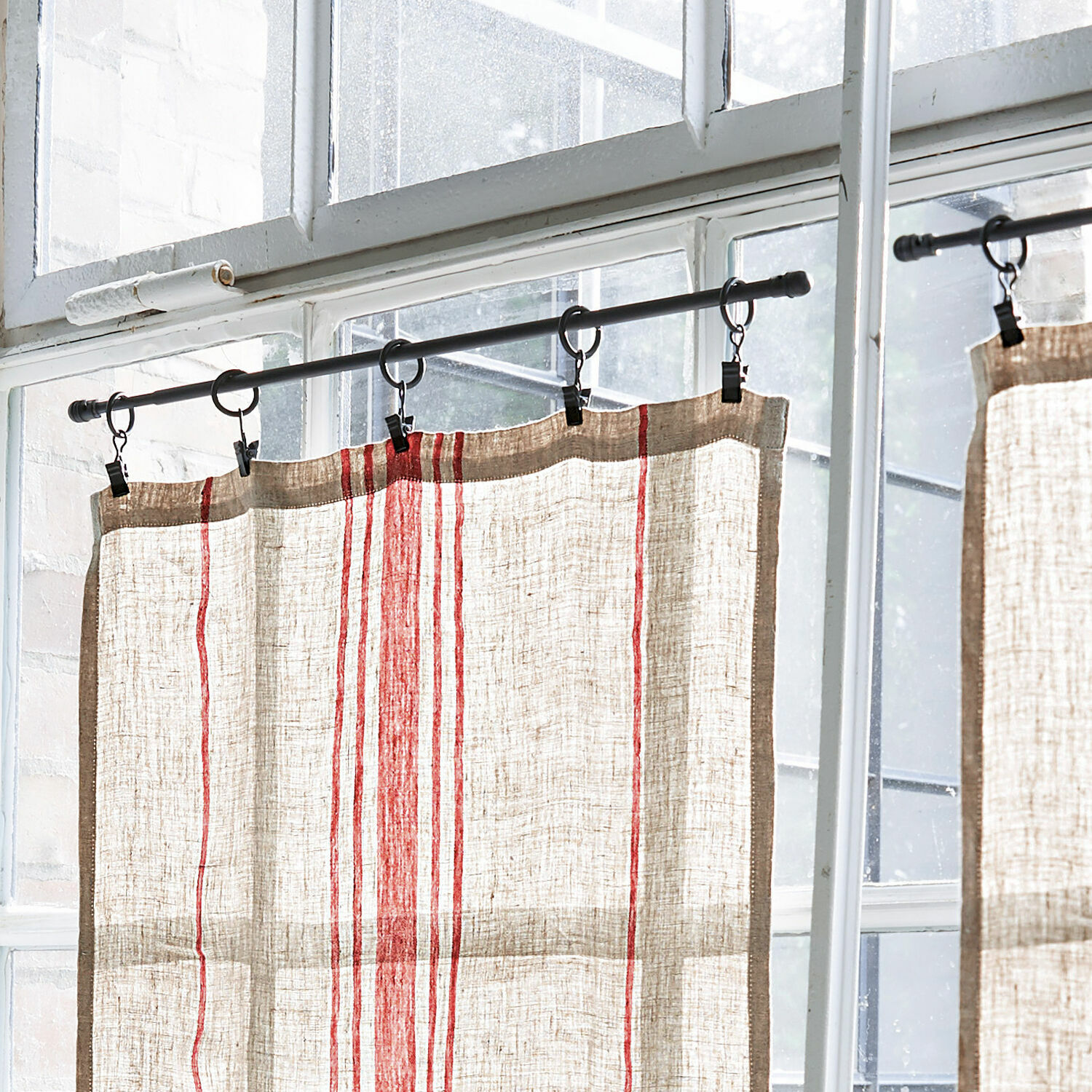 Leinenvorhang in Naturfarbe mit roten Streifen an Metallstange vor dem Fenster hängend