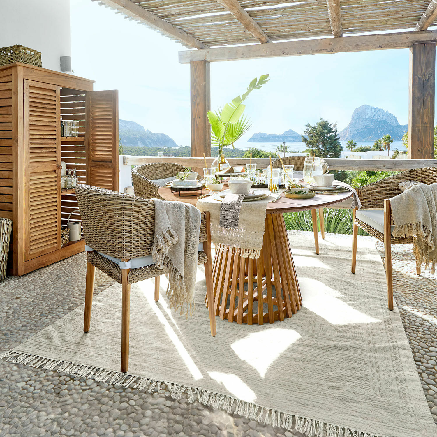 In- & Outdoor-Teppich Savagnac Terrassen-Essbereich mit rundem Holztisch und beigen Rattanstühlen, Meerblick und natürliche Dekoration