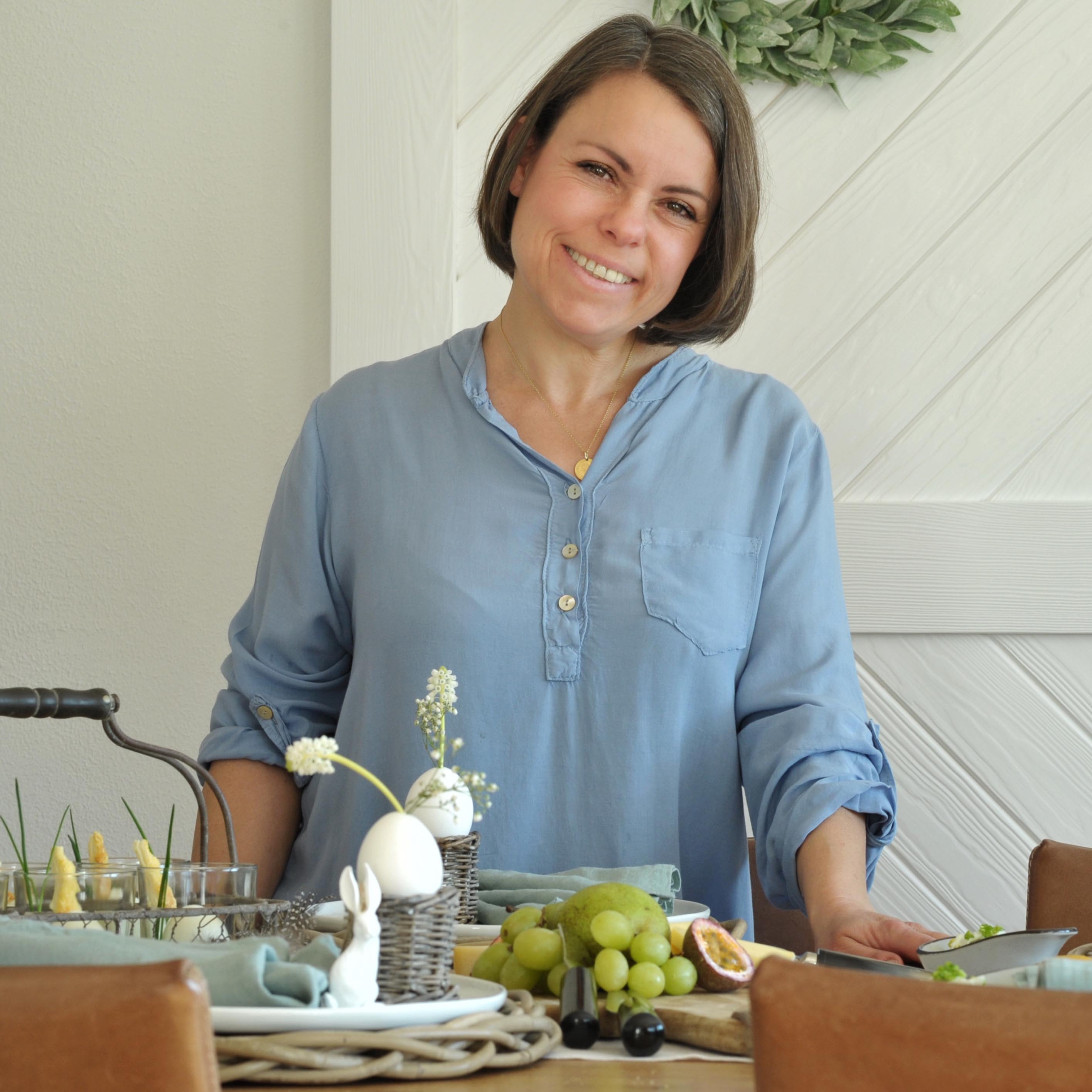 Frau im blauen Hemd am Tisch mit Osterdekoration und Obst zum Brunch
