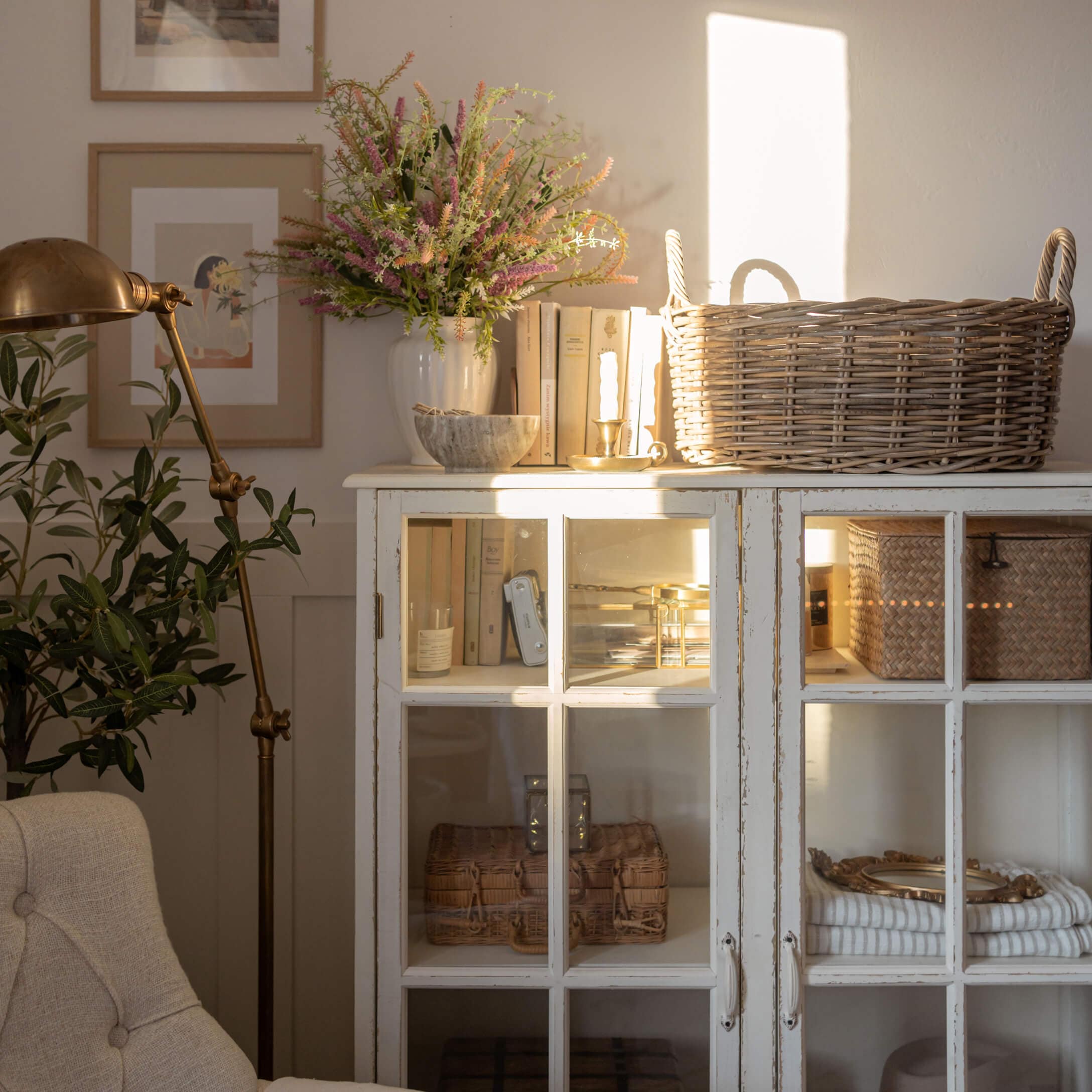 Weißer Holzschrank mit Glastüren, Weidenkorb und Dekorationen in hellem Wohnzimmer