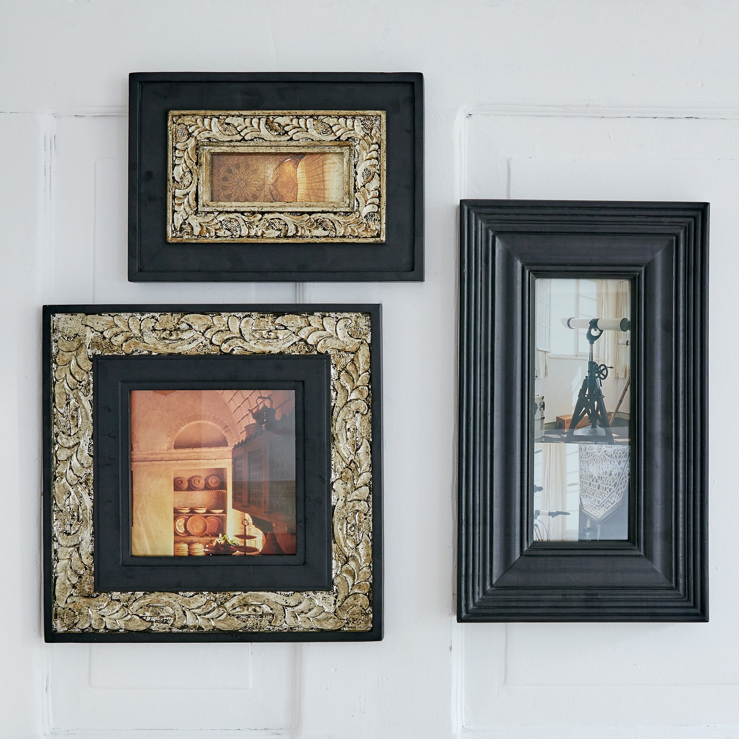 Drei schwarze Bilderrahmen mit goldenen Verzierungen und Vintage-Fotos an weisser Wand