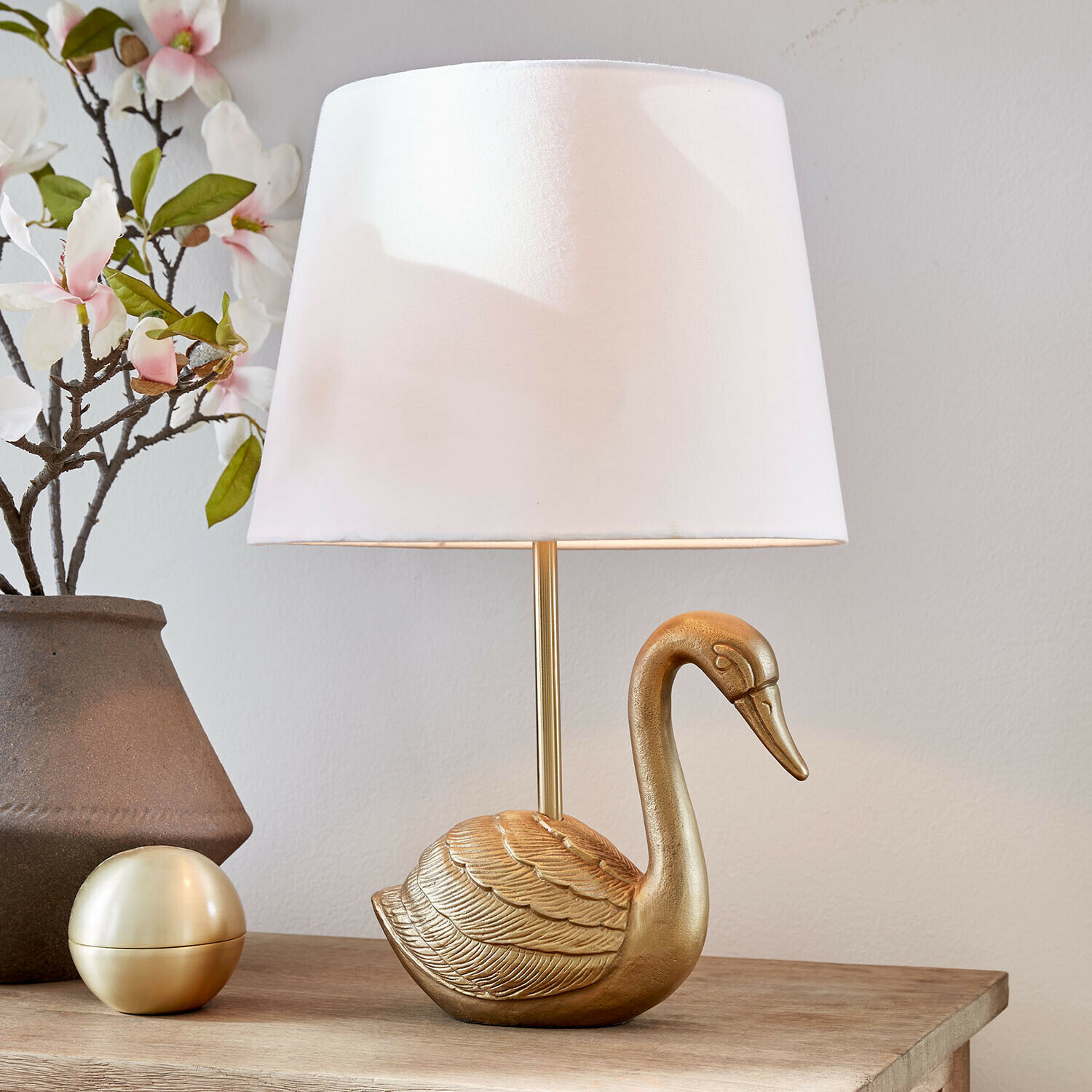 Tischlampe Élégance Dorée Goldene Tischlampe in Schwanform mit weissem Lampenschirm auf Holztisch mit Blumenarrangement