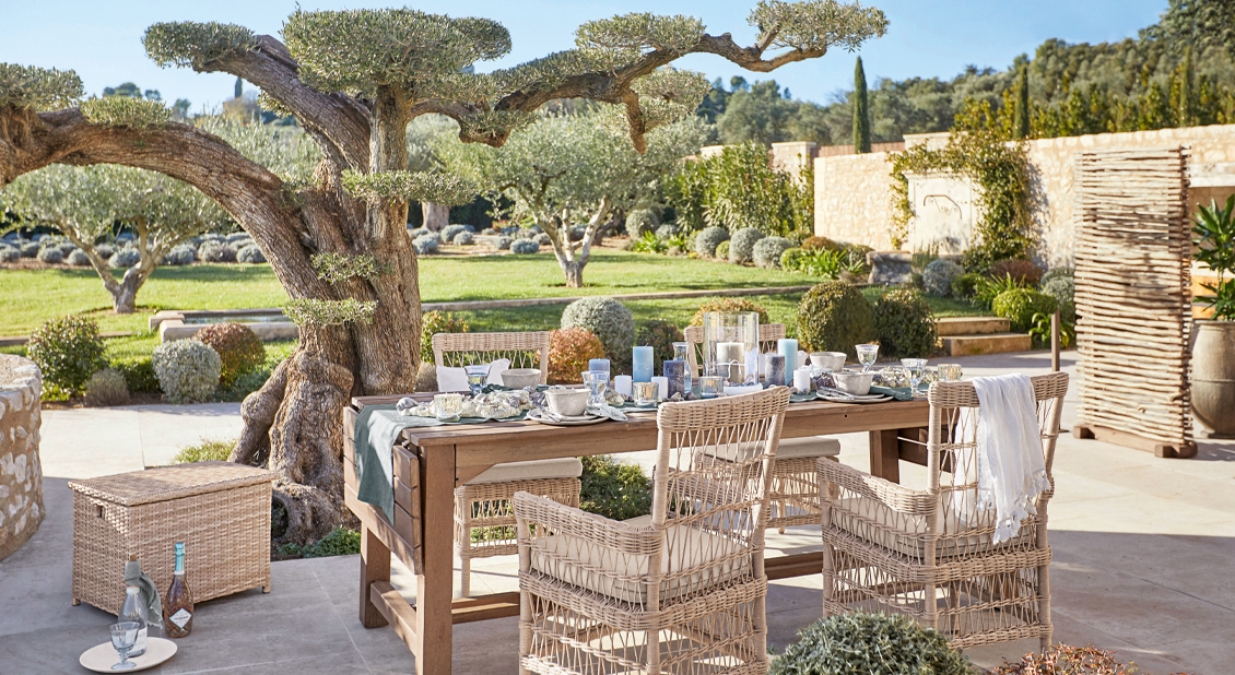 Gartenmöbel-Set aus Holz und natürlichem Rattan auf der Terrasse mit Blick auf den grünen Garten