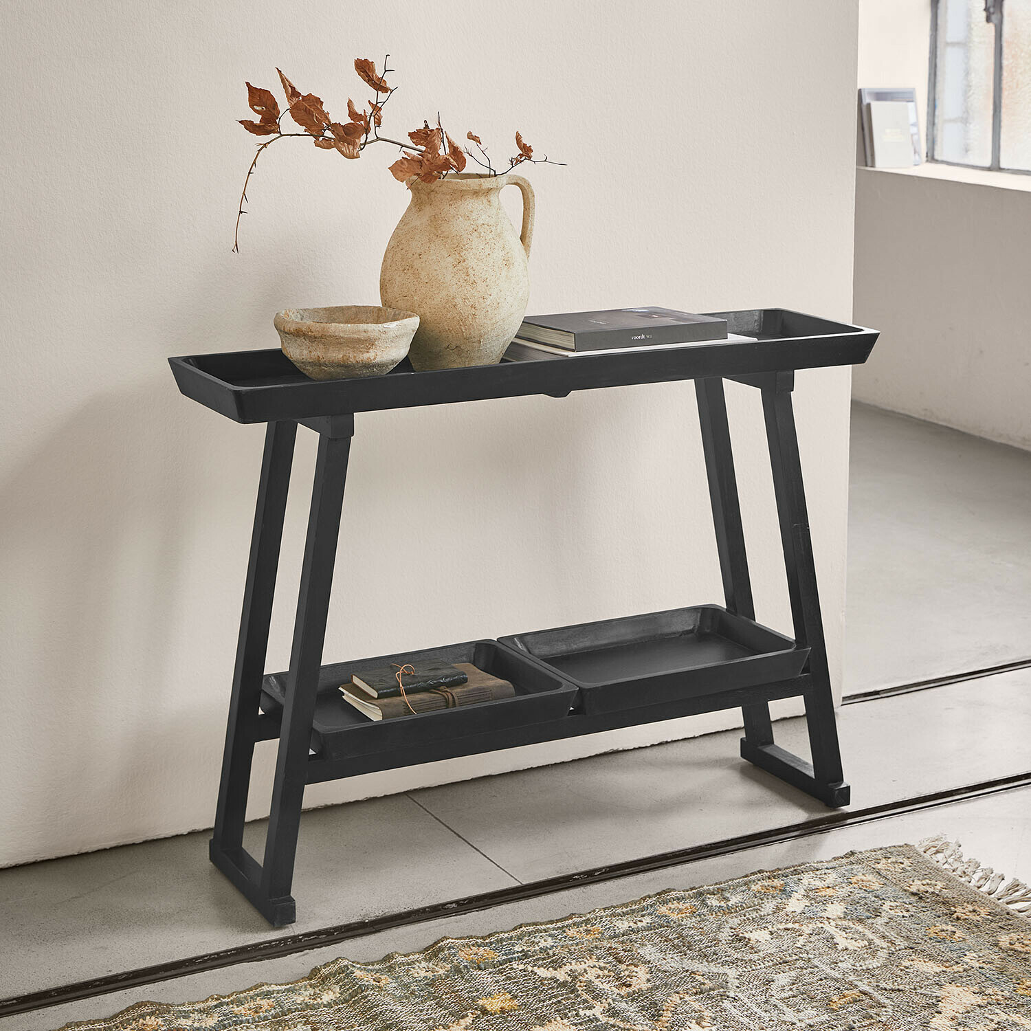 Schwarzer Holzbeistelltisch mit Ablagen, Keramikvase und Büchern in minimalistischem Raum