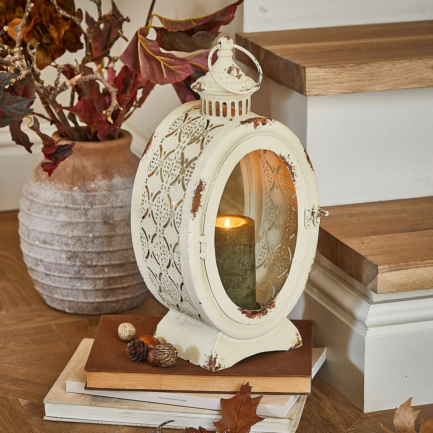 Laterne Sublimelle Vintage-Metalllaterne in Creme mit brennender Kerze und herbstlicher Dekoration auf Büchern