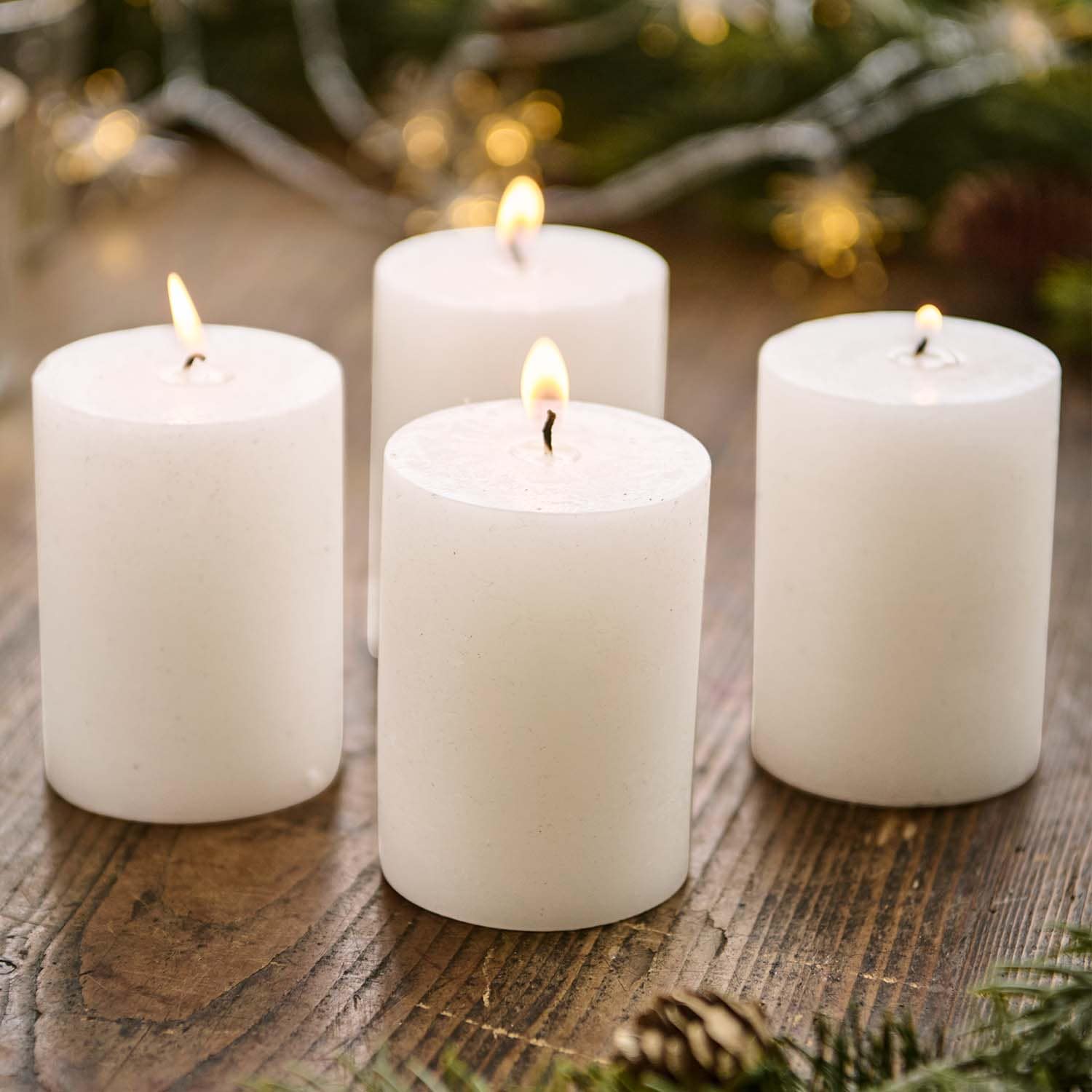 Vier weisse Stumpenkerzen auf Holztisch mit weihnachtlicher Dekoration im Hintergrund