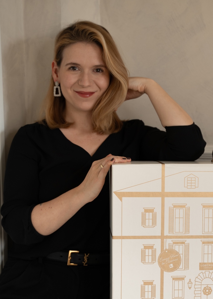 Frau in schwarzer Bluse mit Geschenkbox, bedruckt mit Hausgrafik für Weihnachten