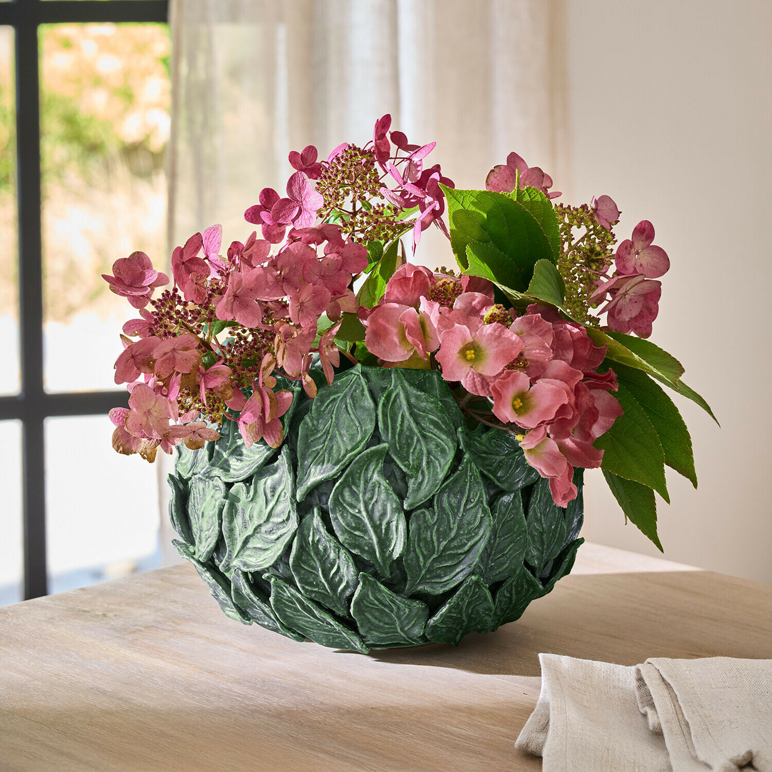 Grüne Blatt-Dekovase mit rosa Blumen auf Holztisch in hellem Raum als Wohnaccessoire