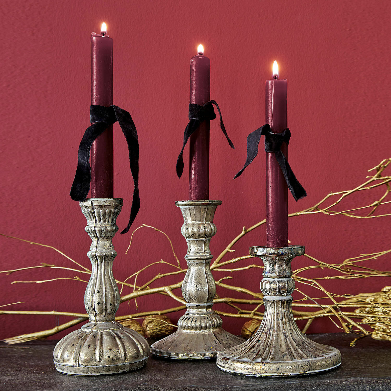 Kerzenständer 3er Set Bretagne Drei dekorative Metallkerzenhalter mit bordeauxroten Kerzen und schwarzen Bändern vor dunklem Hintergrund