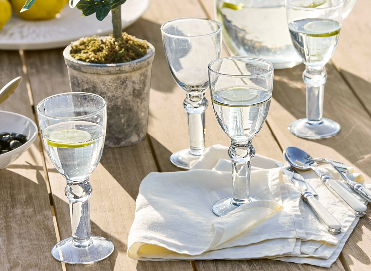 Wassergläser mit Zitrone auf Holztisch mit weisser Serviette und Besteck, mediterraner Stil