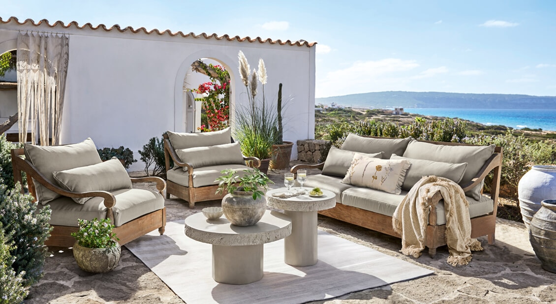 Gartenmöbel-Set aus Holz mit beigen Polstern auf steinerner Terrasse mit Meerblick
