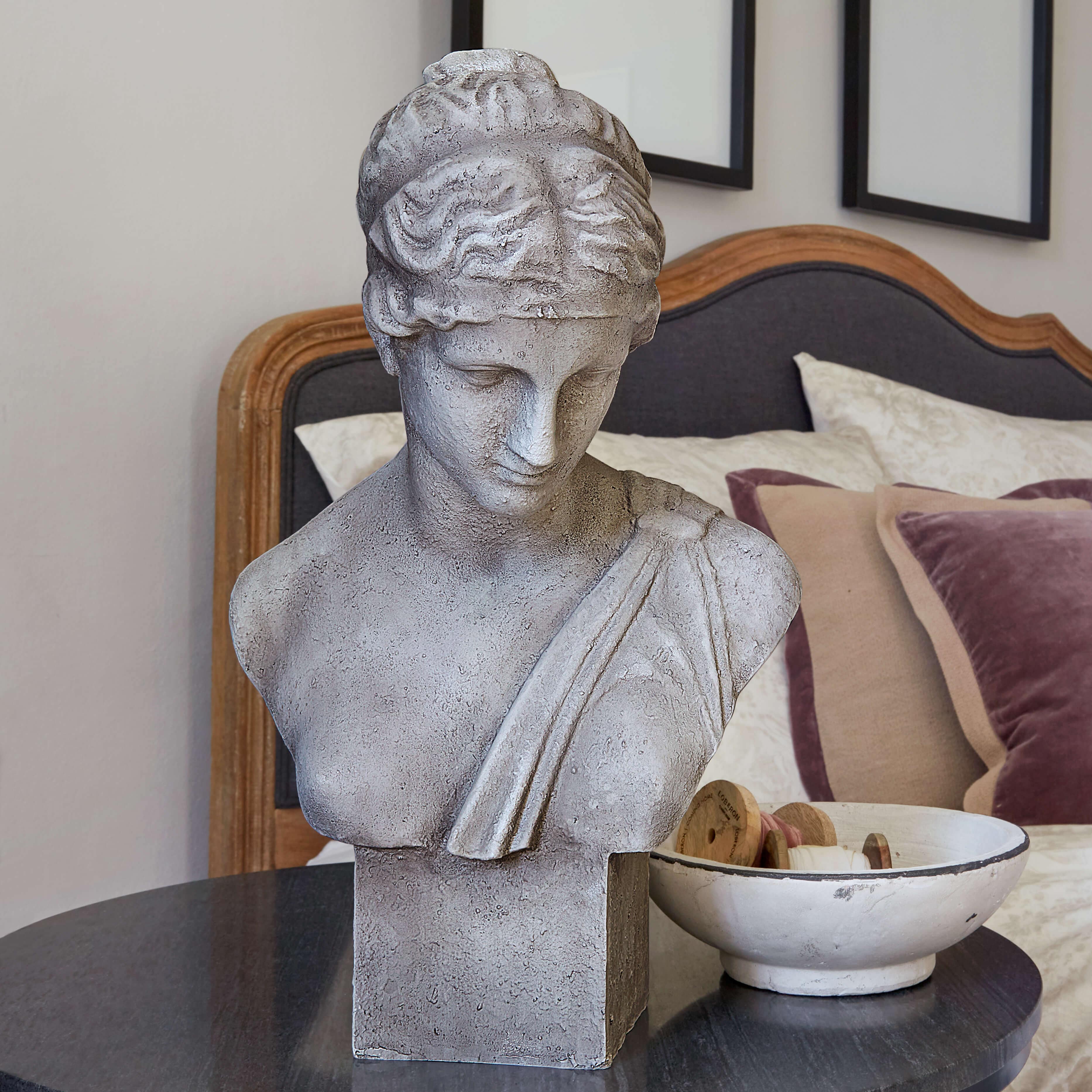 Graue Steinskulptur-Büste auf Tisch neben weisser Schale mit Holzspulen im Schlafzimmer