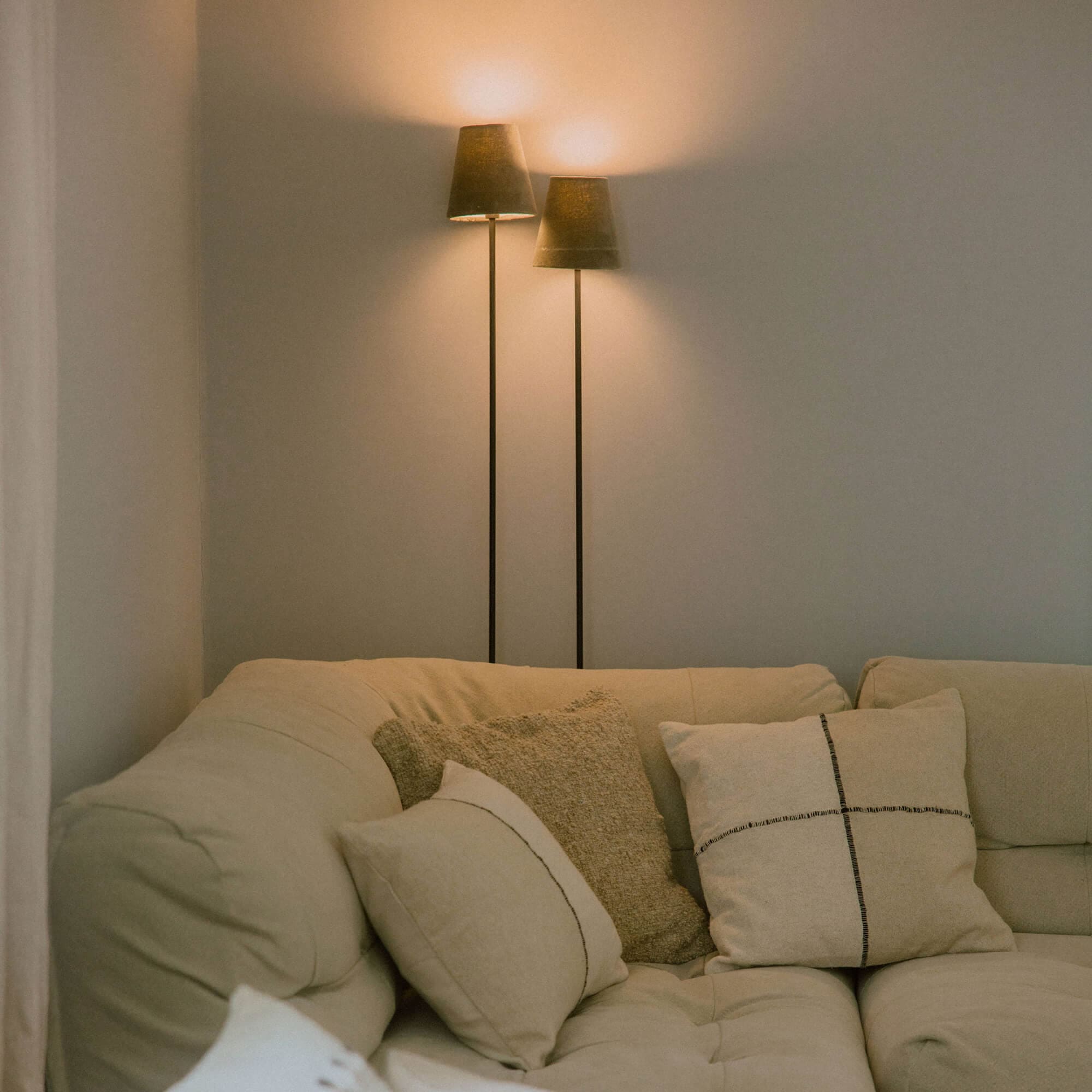 Beiges Sofa mit weichen Kissen und zwei Stehlampen mit dunklen Lampenschirmen im Wohnzimmer