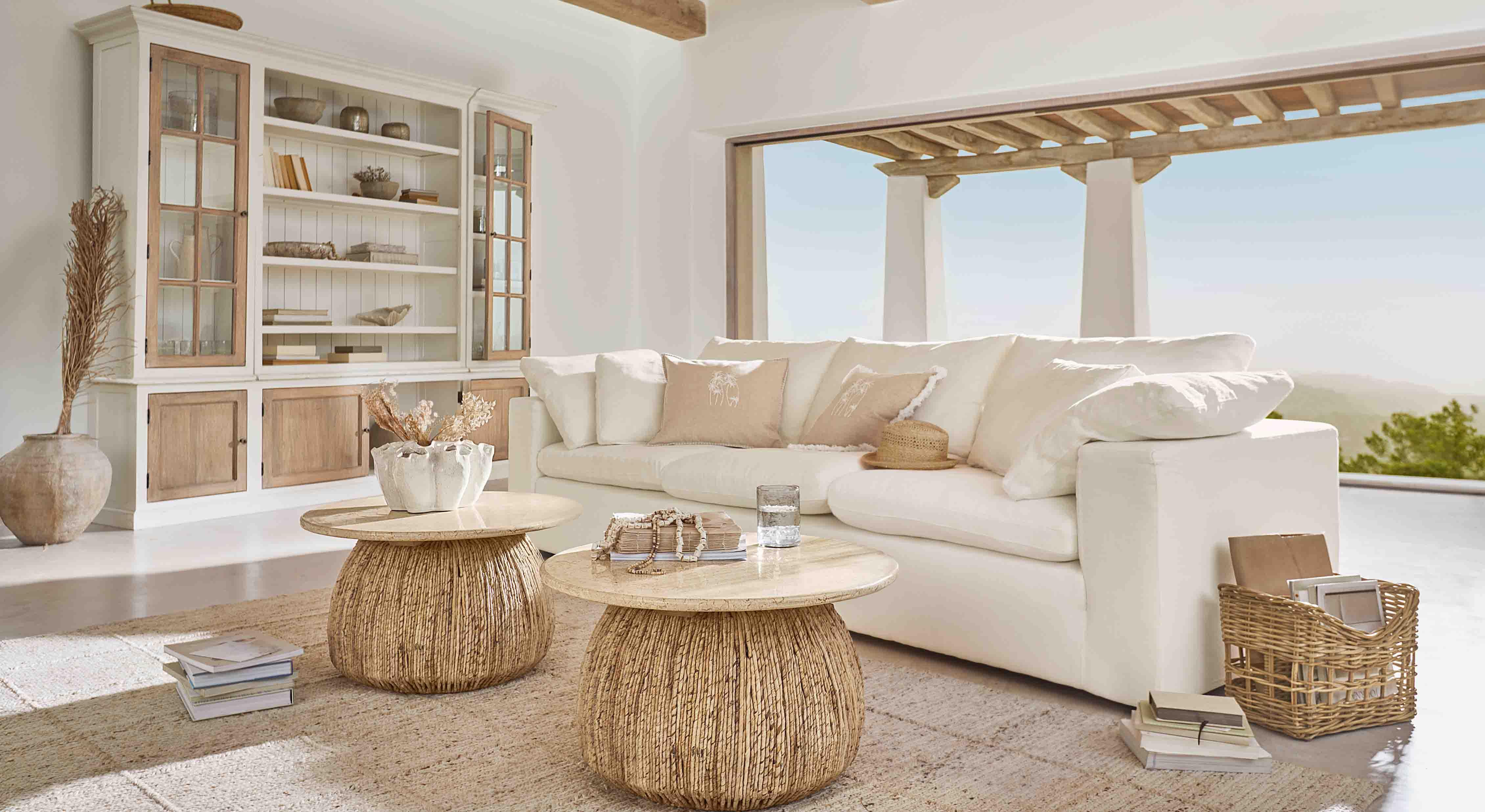 Gemütliches Wohnzimmer mit weissem Sofa und zwei runden Couchtischen aus Naturholz und Rattan