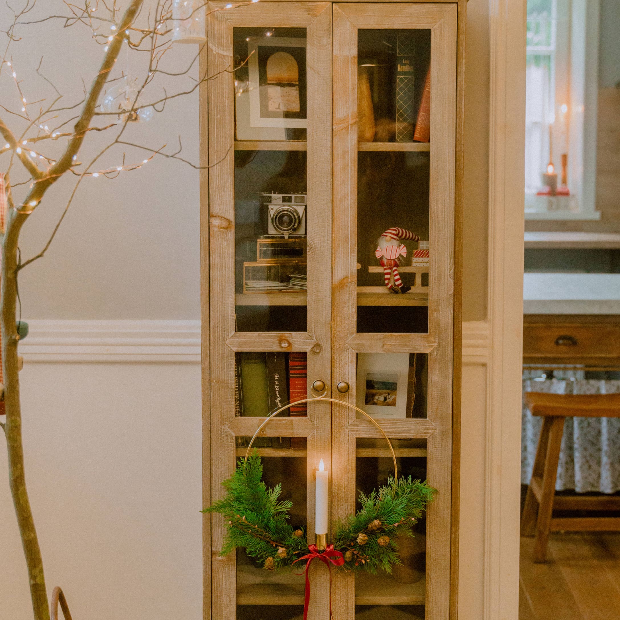 Holzvitrine mit Glastüren und Weihnachtskerzenhalter mit grünen Zweigen und roter Schleife