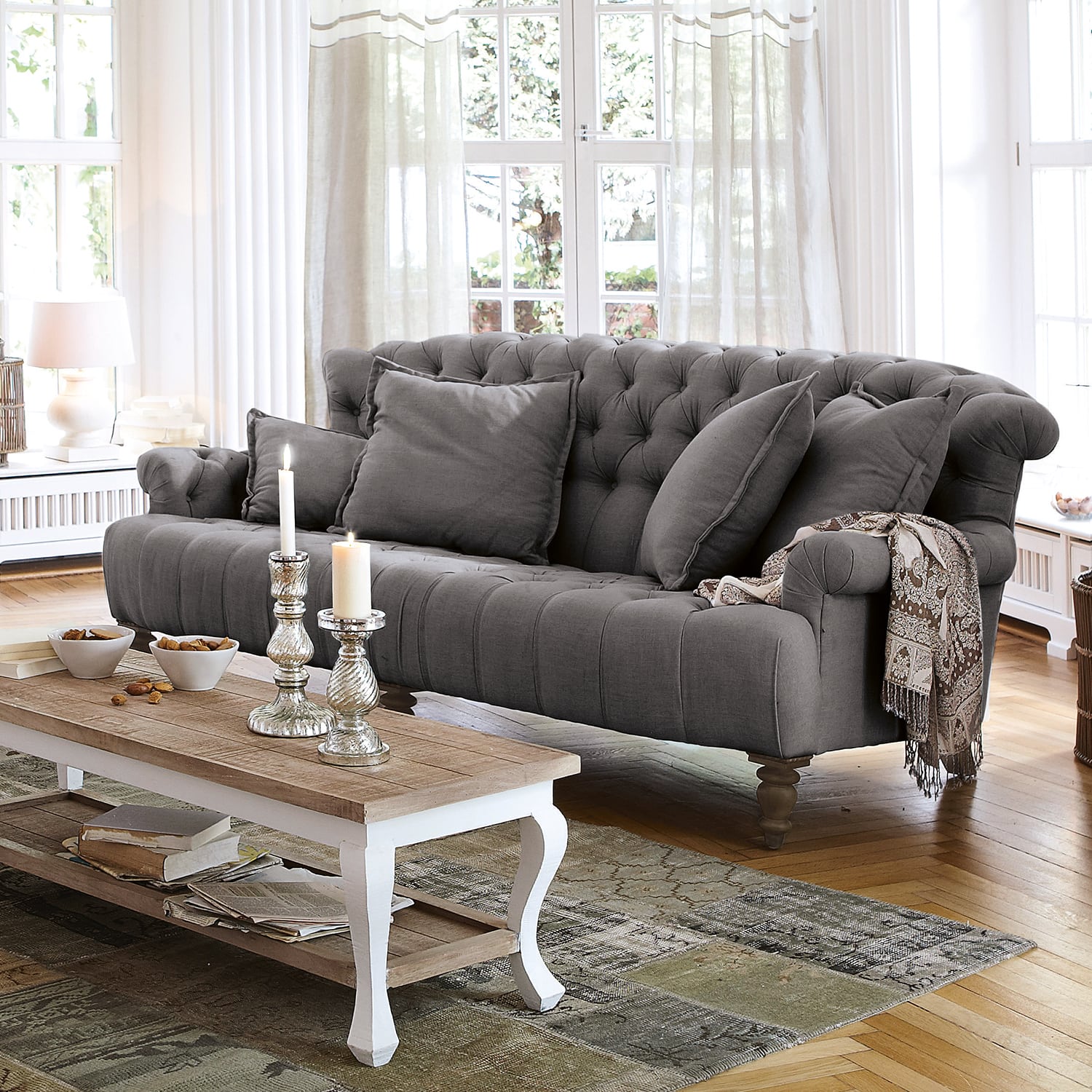 Grau gepolstertes Stoffsofa mit Kissen und dekorativem Plaid in hellem Wohnzimmer mit Holzboden