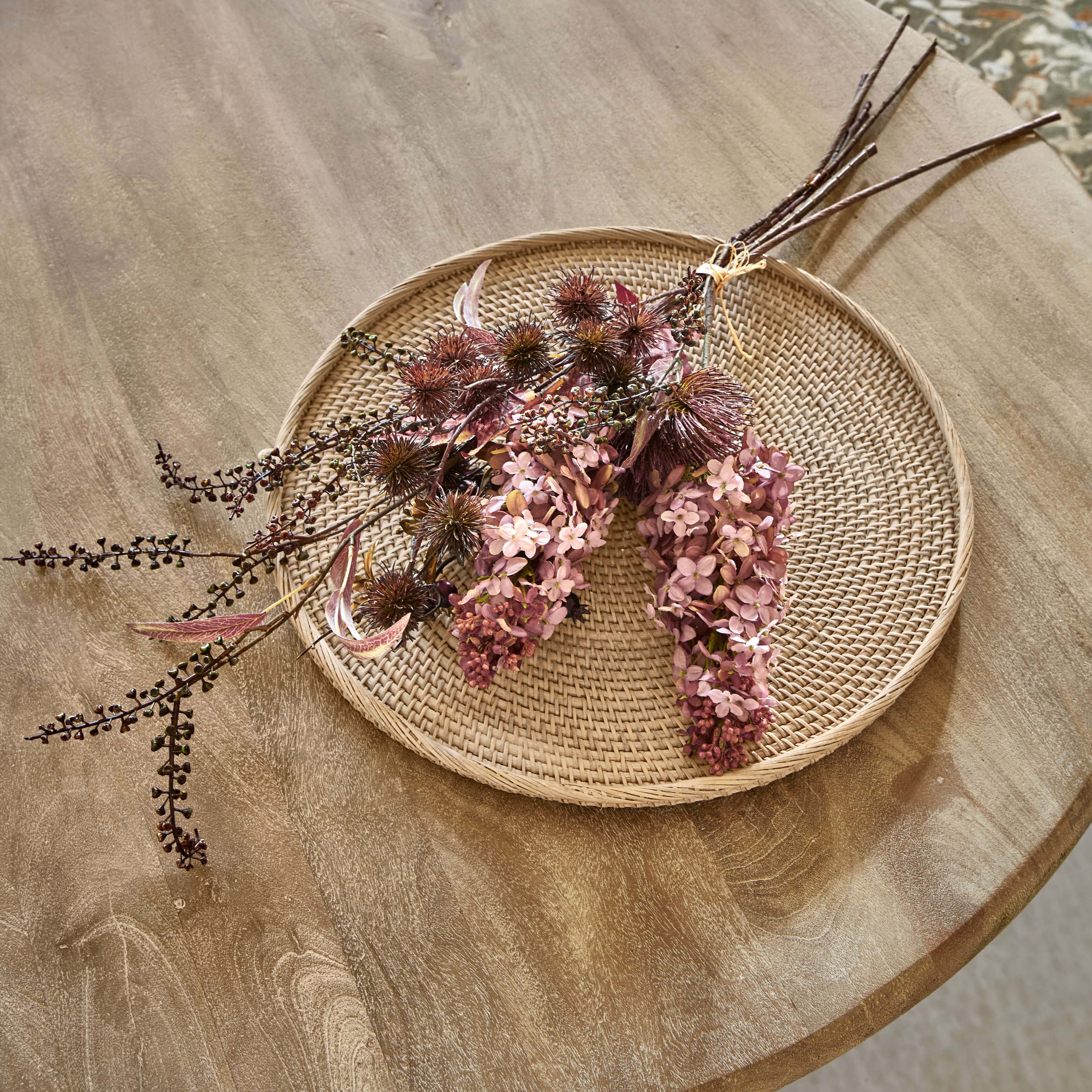 Dekorativer Trockenblumenstrauß in Rosa- und Brauntönen auf geflochtenem Rattanteller als Wohnaccessoire