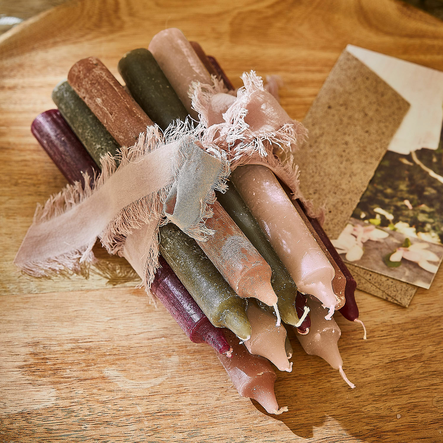 Kerze 12er Set Bauceau Bündel bunter Stabkerzen aus Naturwachs mit rosa Band auf Holztisch gebunden