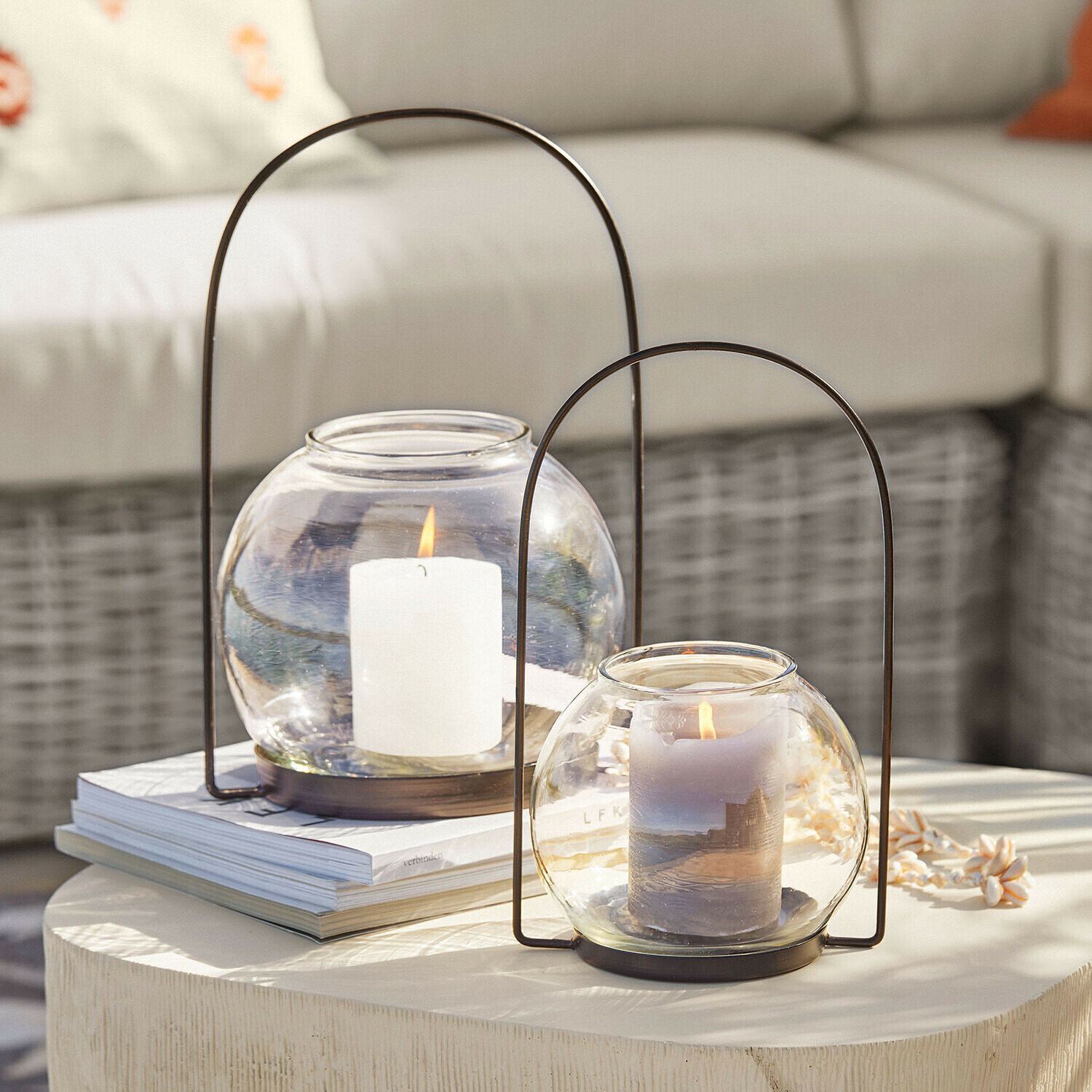 Zwei Glaslaternen mit Metallgriffen und brennenden Kerzen auf hellem Dekotisch