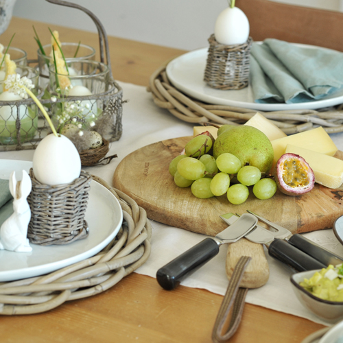 Osterbrunch-Tisch mit Holzbrett, Trauben, Birne, Käse und Eierdekorationen aus Weideholz
