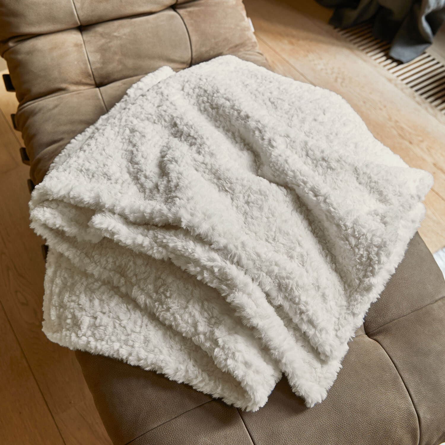 Weiche weisse Kuscheldecke aus Plüsch auf braunem Sessel, ideal fürs Wohnzimmer