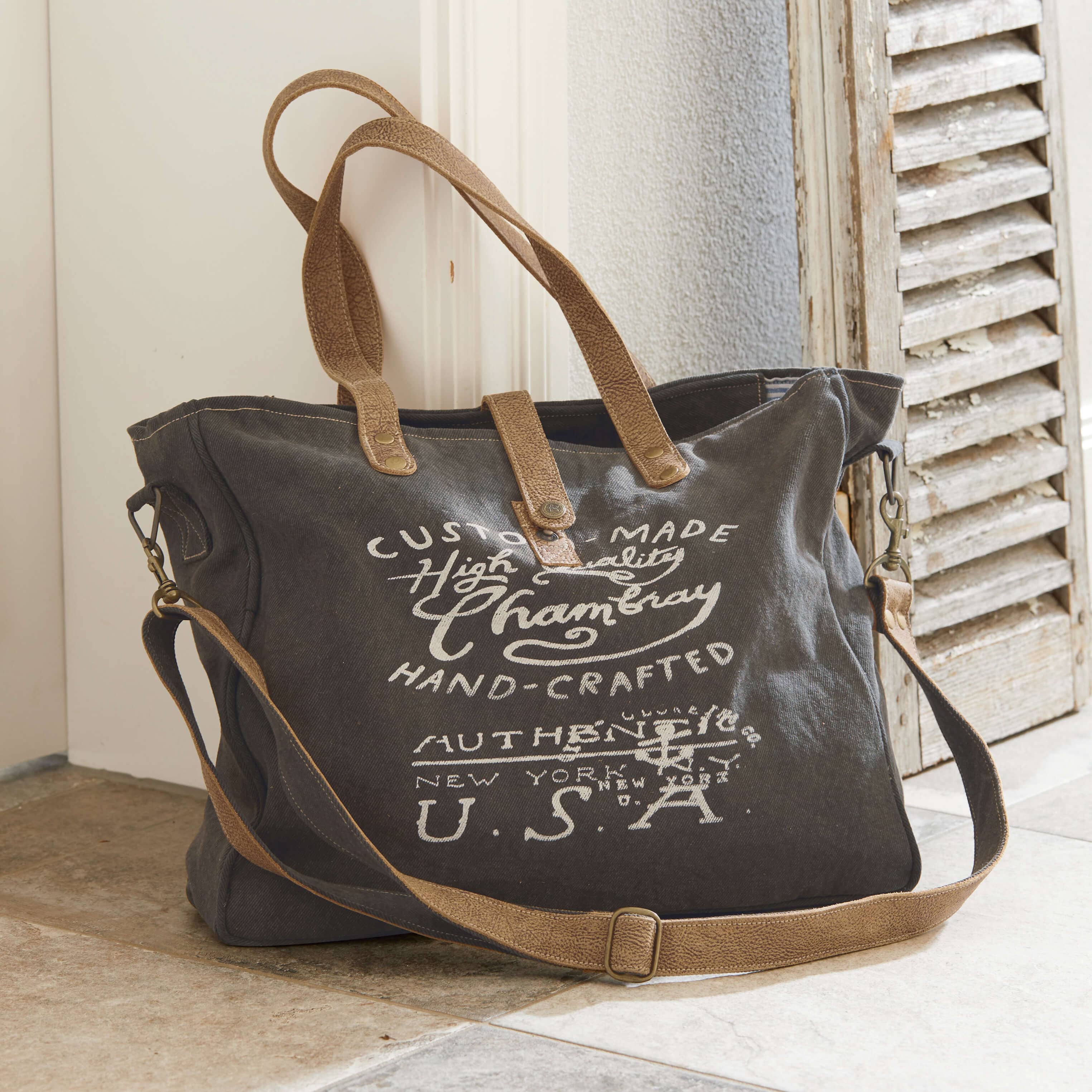 Dunkelgraue Stofftasche mit braunen Ledergriffen und weißem Textdruck, Reisetasche