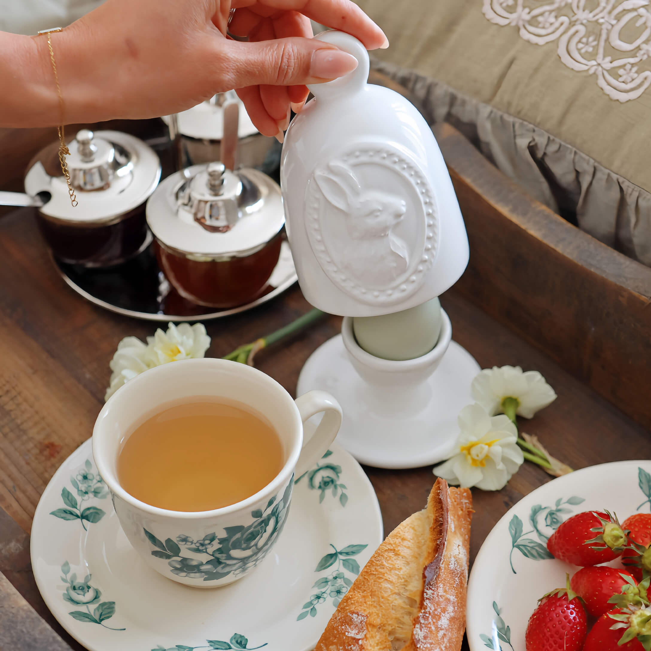 Weisser Keramikbehälter mit Hasenmotiv auf Frühstückstisch mit Tee und Erdbeeren