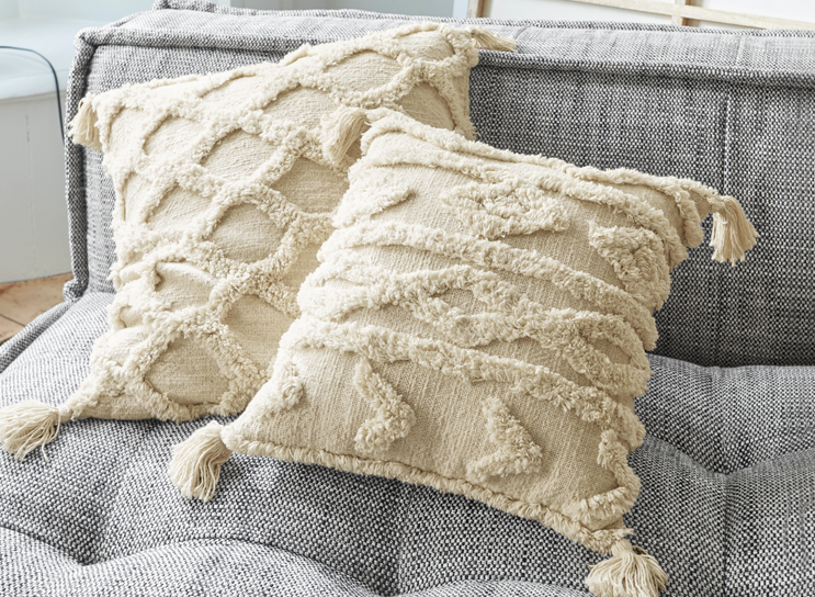 Beige dekorative Kissen mit Fransen und geometrischem Muster auf grauem Sofastoff