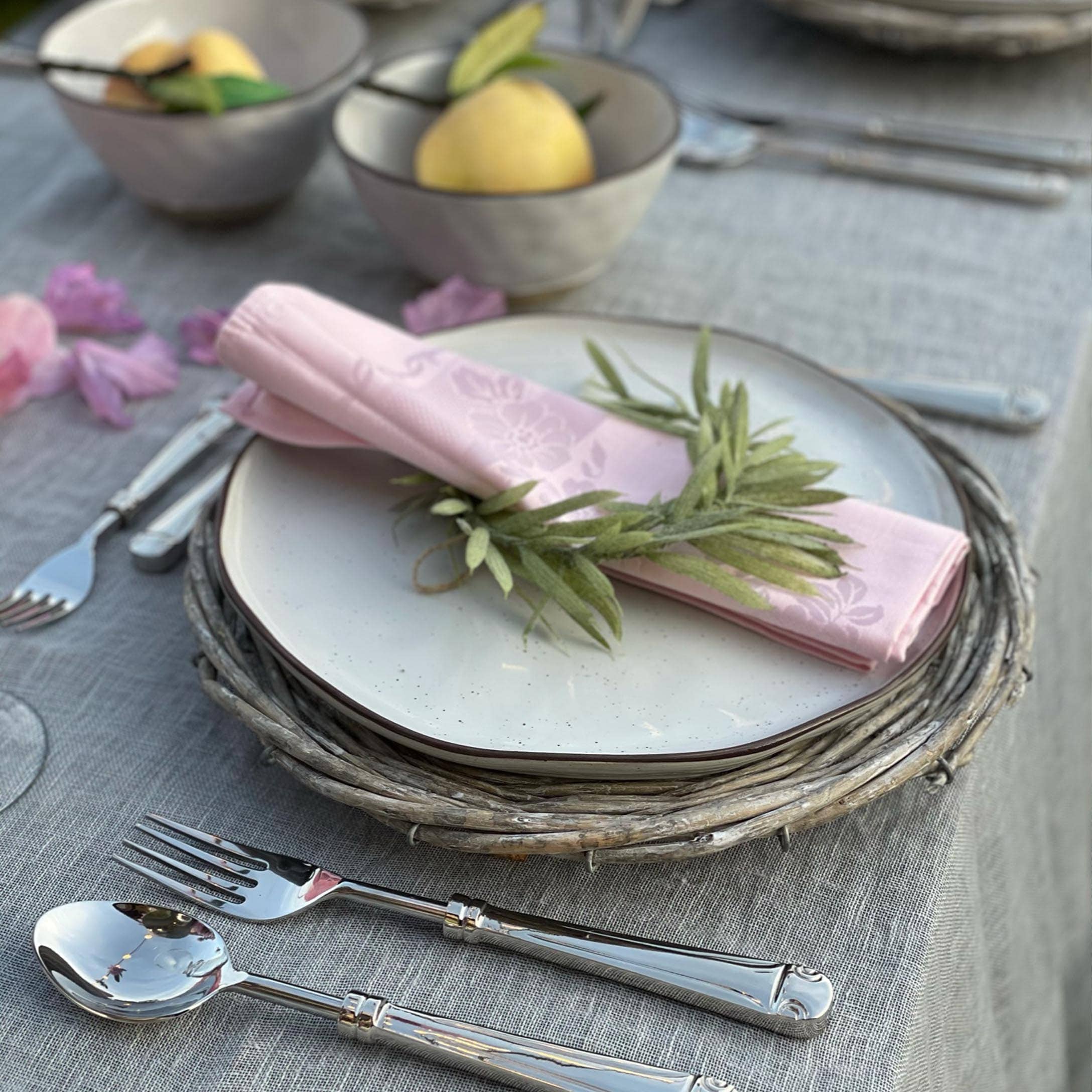 Elegantes Gedeck mit weissem Teller auf Weidenuntersetzer und rosa Serviette mit grünen Blättern