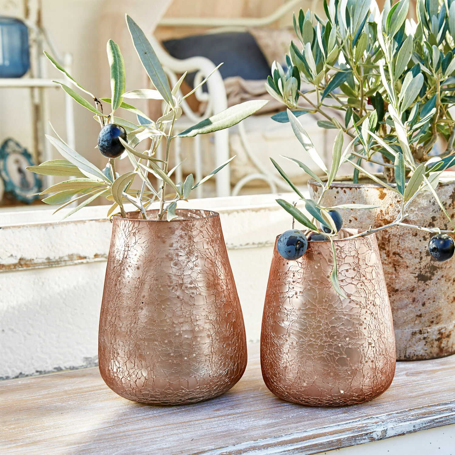 Zwei kupferfarbene Glasvasen mit rissiger Struktur und Olivenzweigen auf dem Holztisch