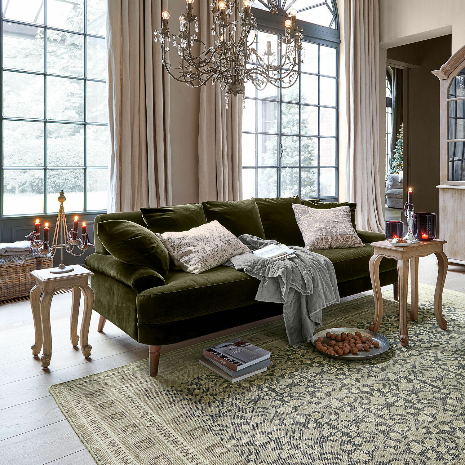 Sofa Rivermere Grünes Samtsofa mit Kissen und grauer Decke im hellen Wohnzimmer mit grossen Fenstern