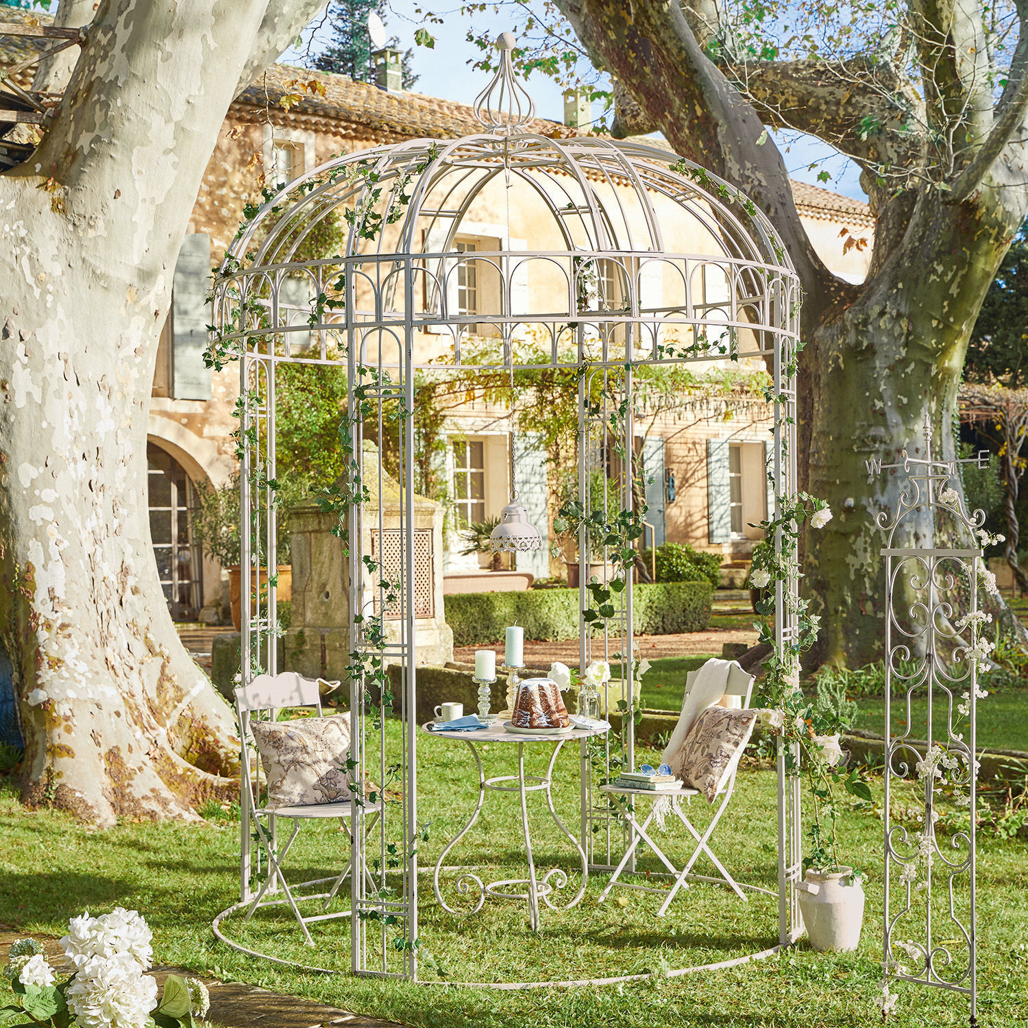 Pavillon Iolanda Weisse Metall-Gartenlaube mit Stühlen und Tisch auf dem Rasen, dekoriert mit grünem Efeu