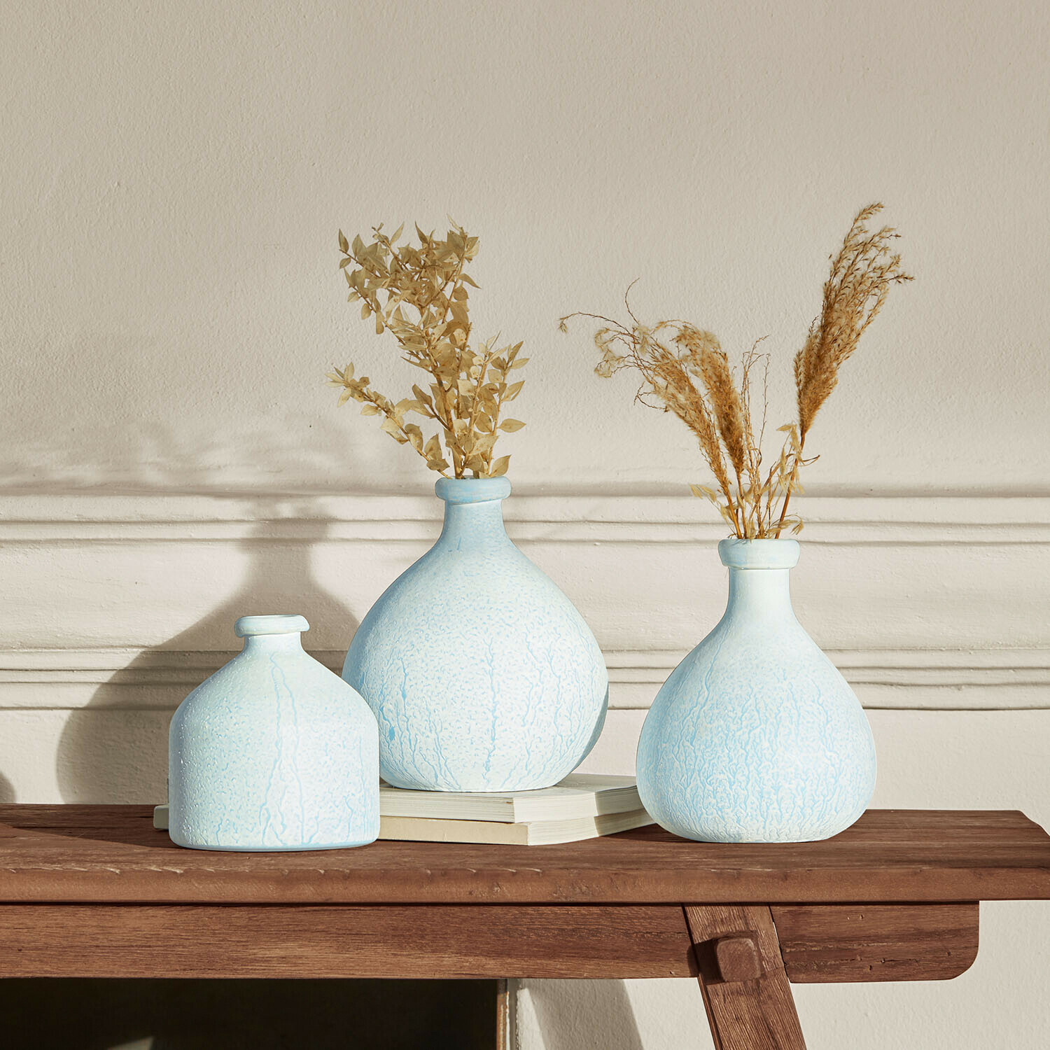 Set mit drei hellblauen Keramikvasen und getrockneten Pflanzen auf Holztisch zur Wohnraumgestaltung