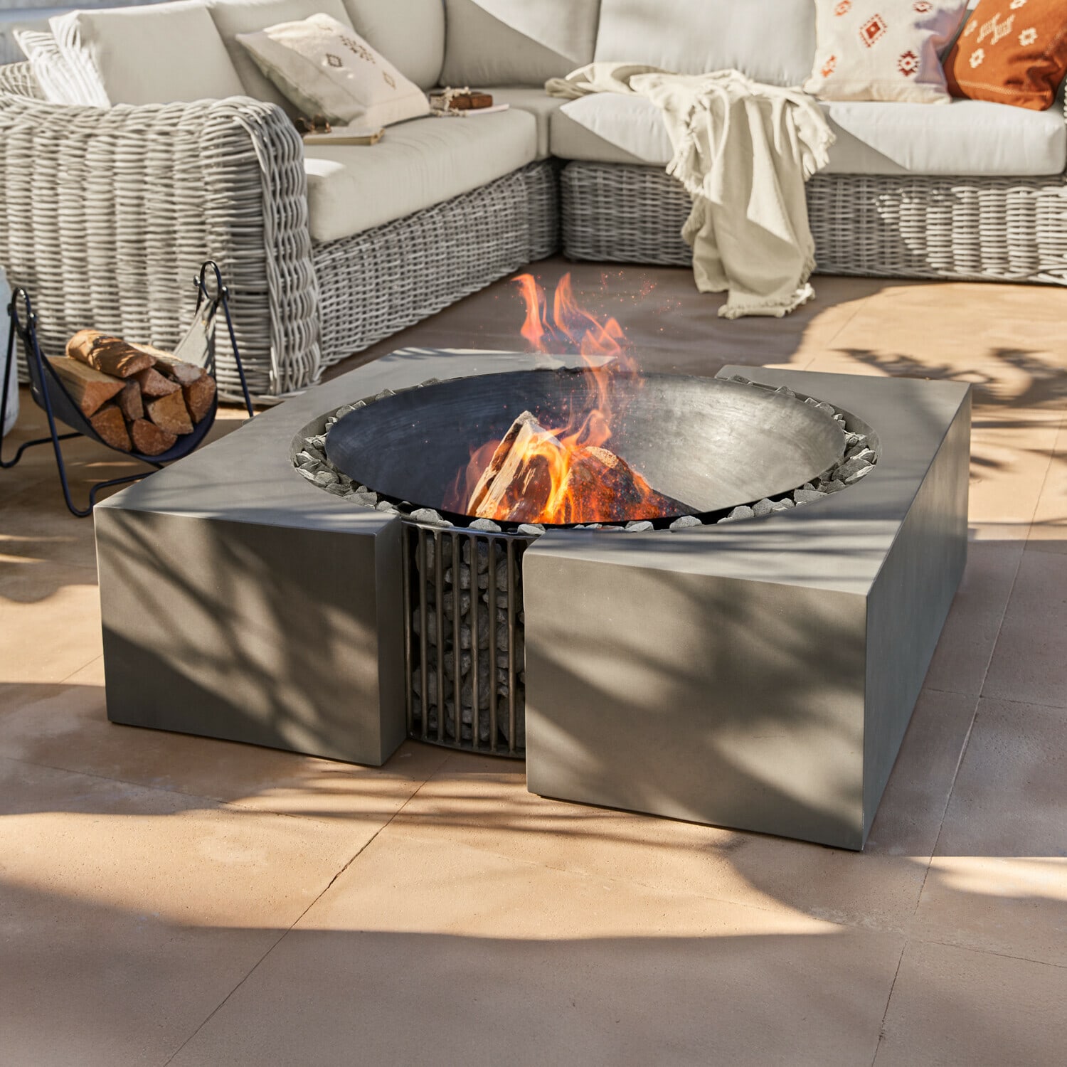 Feuerstelle Charonville Moderne Feuerstelle aus schwarzem Metall mit Steinen auf Terrasse neben Rattansofa mit Kissen