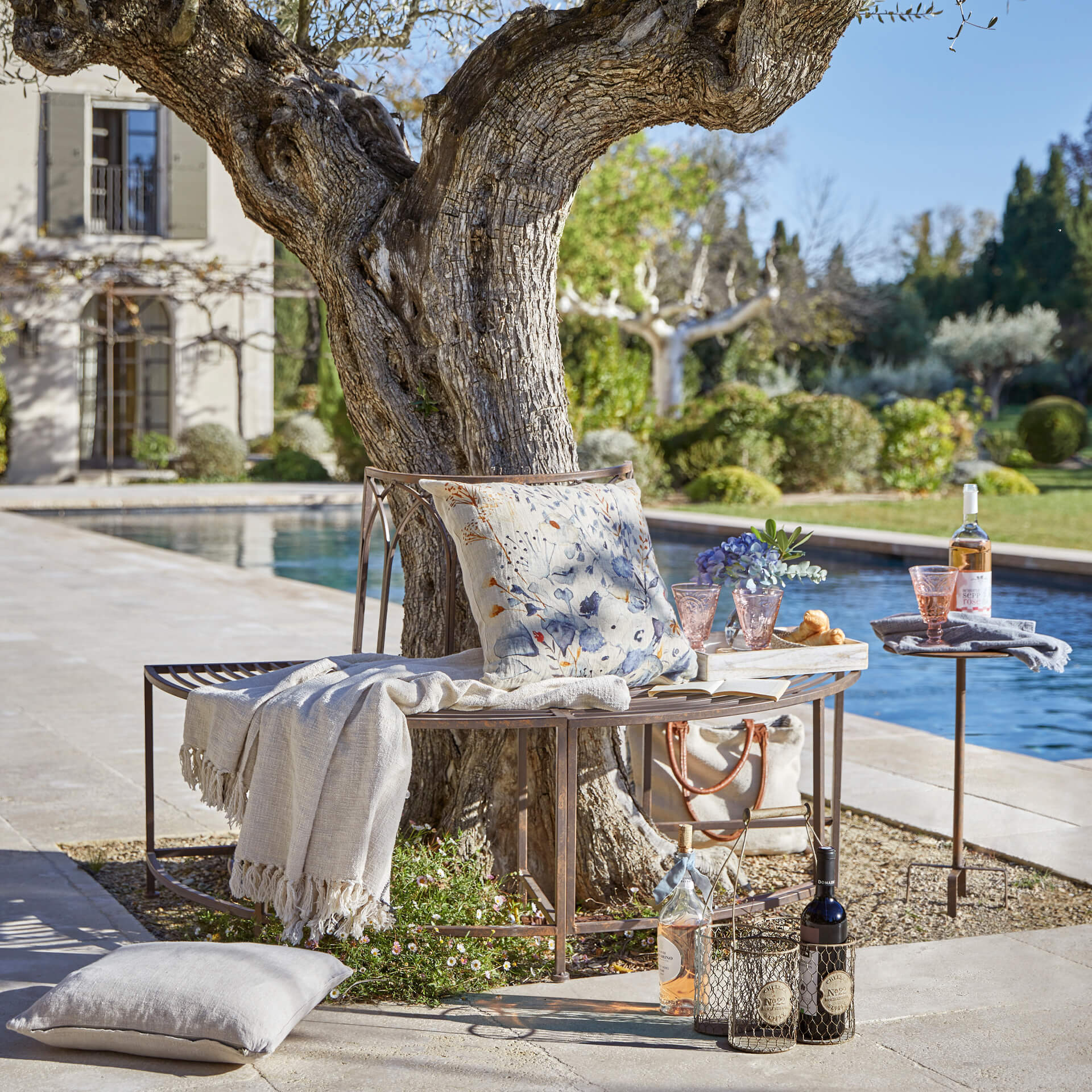 Metallbank in Kupferfarbe unter Baum mit Kissen und Decke beim Pool im Garten