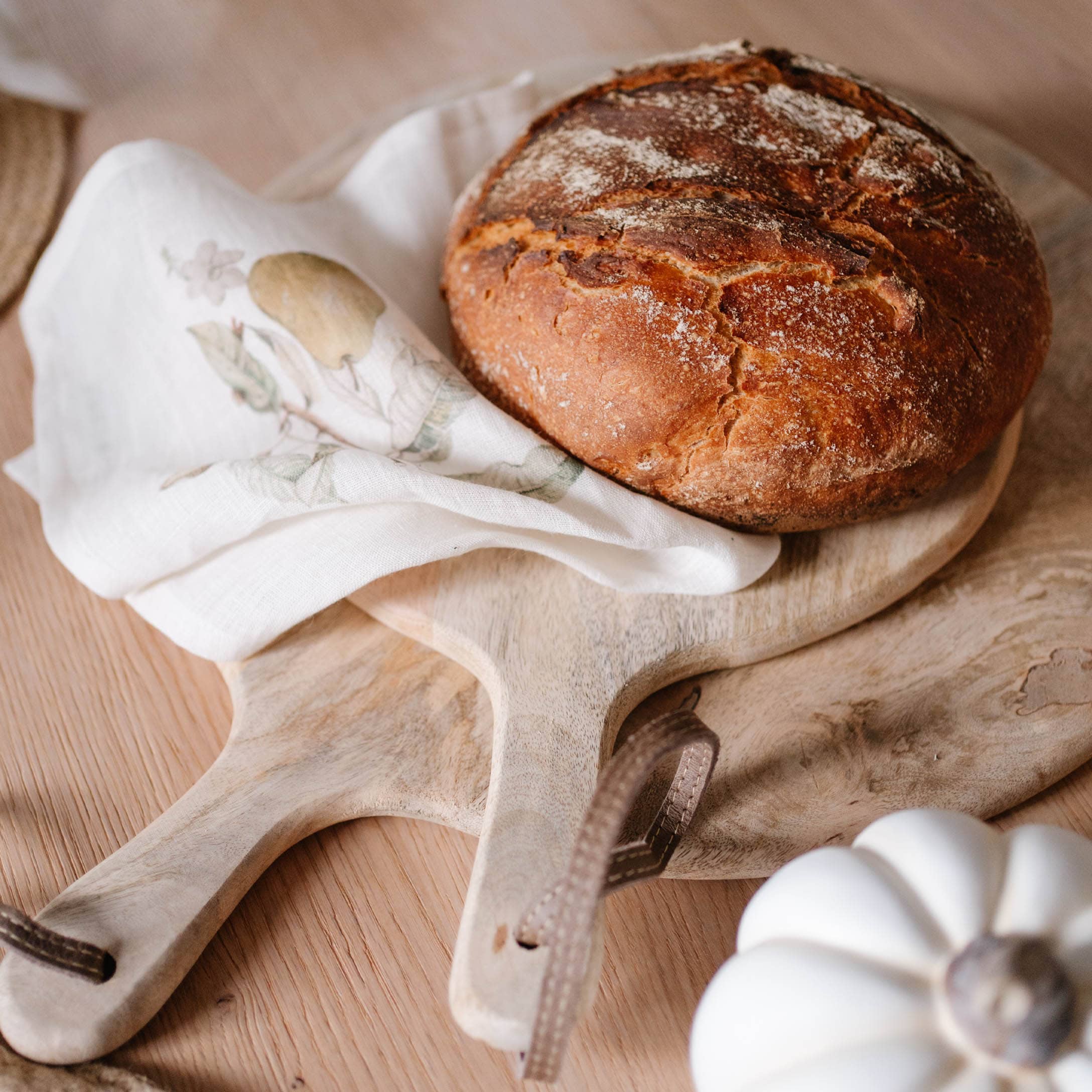 Frisches Brot auf Holzbrett mit Leinentuch und weissem Dekokürbis auf Holztisch