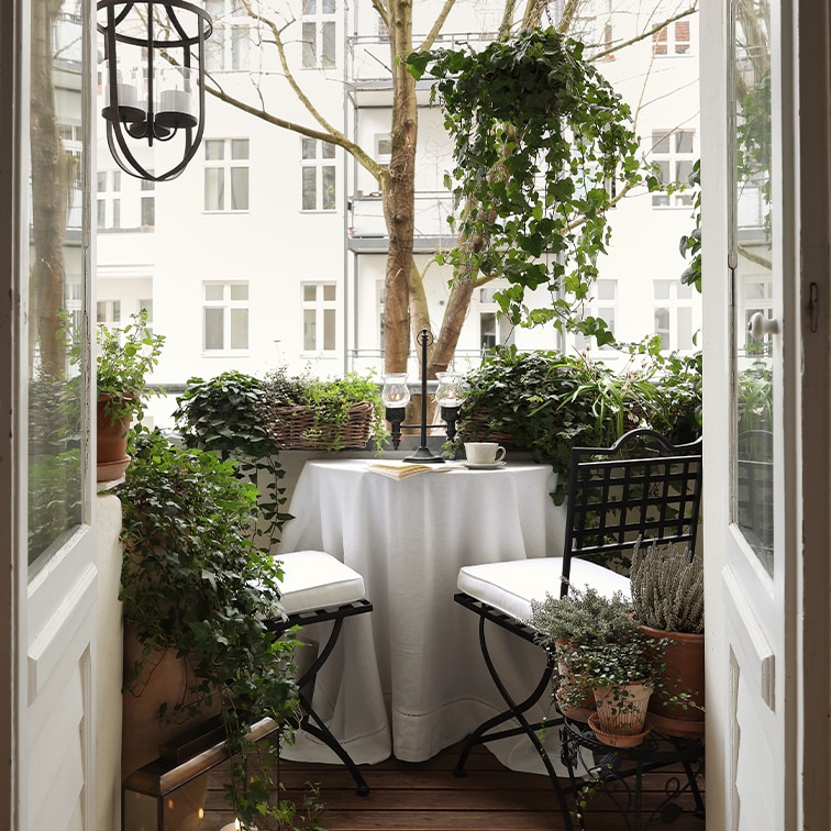 Gemütlicher Balkon mit weissem Tisch, schwarzen Stühlen und grünen Pflanzen zum Entspannen.