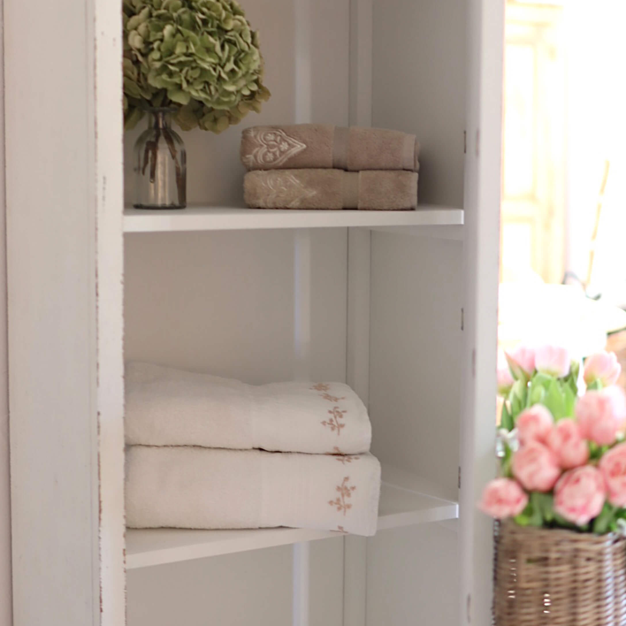 Weiche Baumwollhandtücher in Beige und Weiss mit feiner Stickerei auf weissem Regal