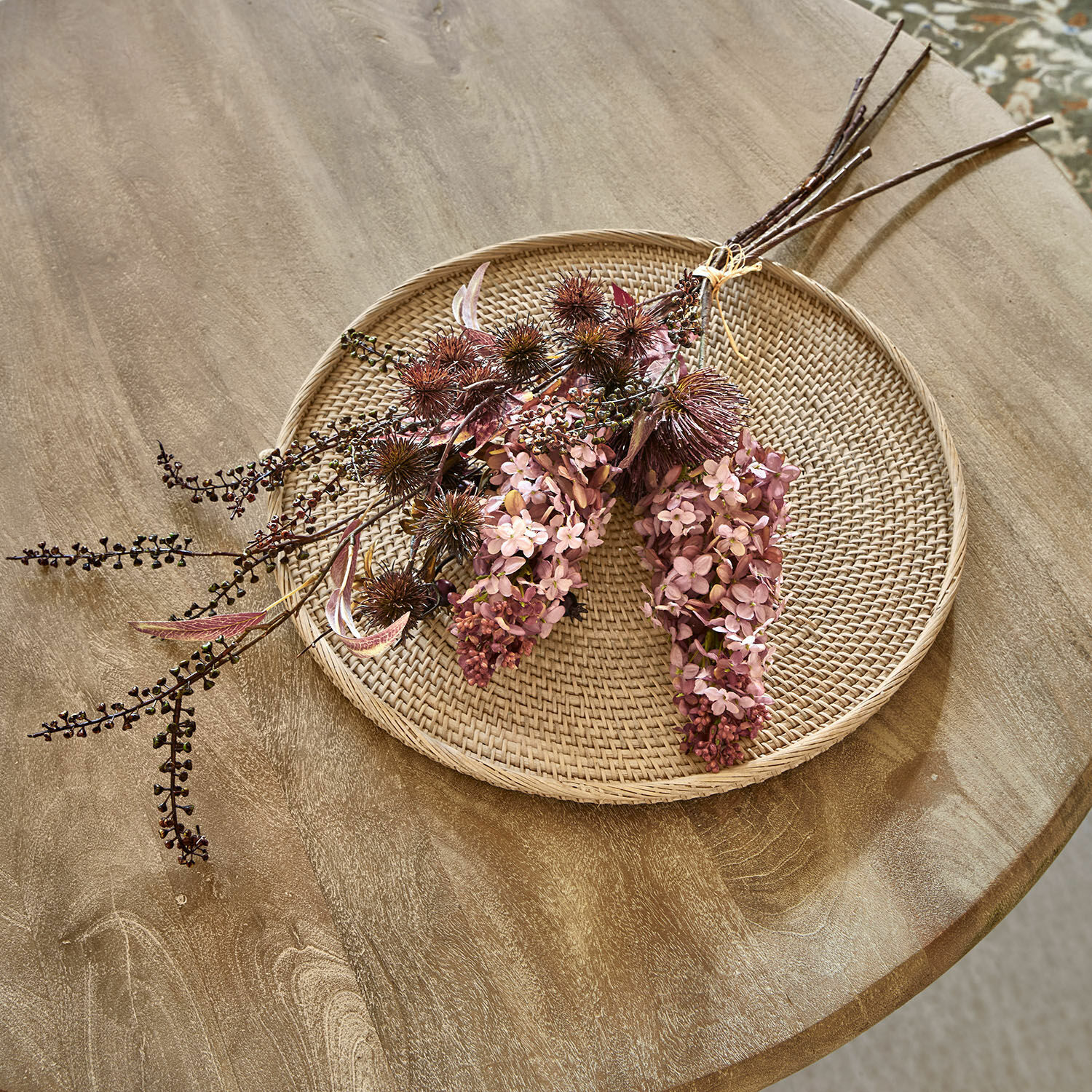 Dekorativer Trockenblumenstrauss in Rosa- und Brauntönen auf geflochtenem Rattantablett als Dekoration