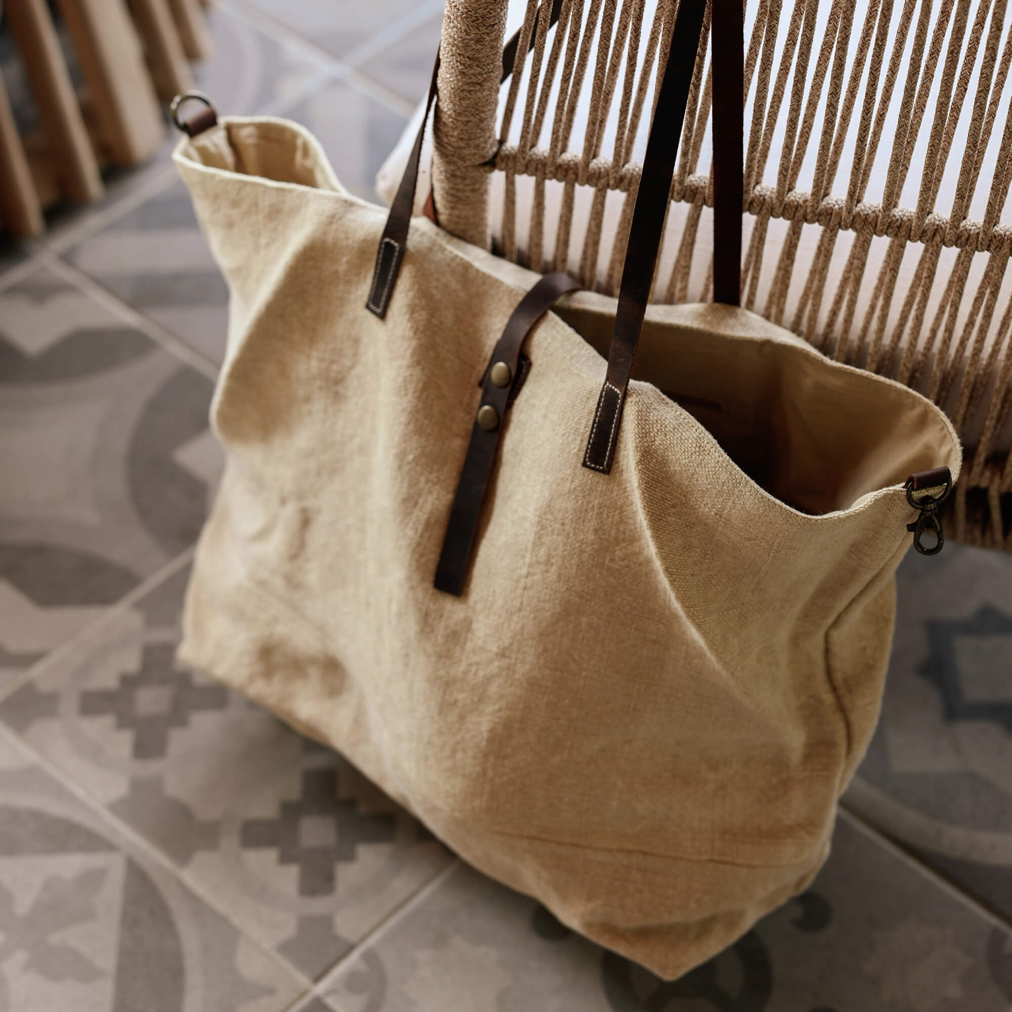 Beige Stofftasche mit dunkelbraunen Ledergriffen auf gemustertem Plattenboden