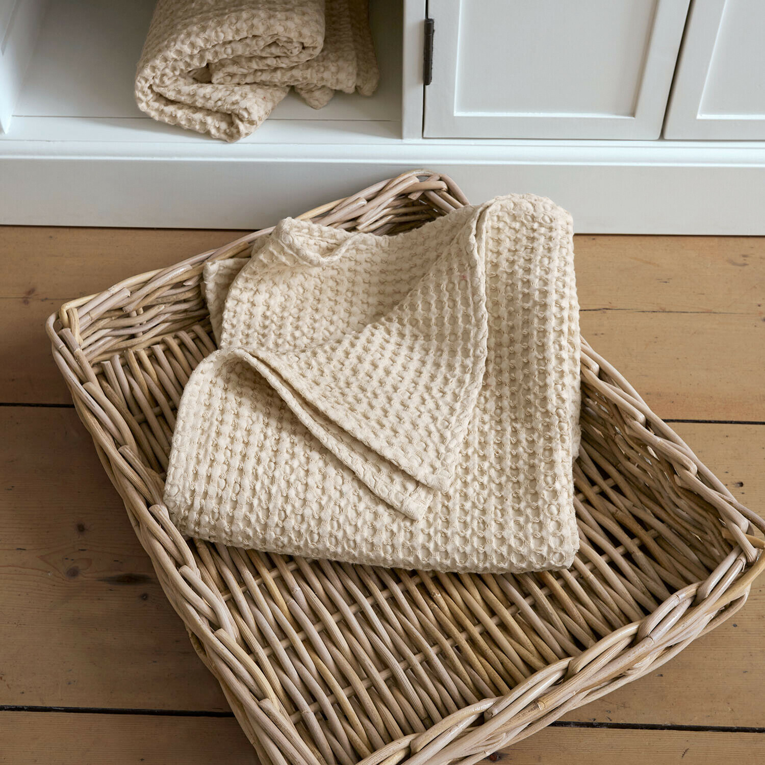 Beige Baumwoll-Waffeldecke in einem Weidenkorb auf hellem Holzboden