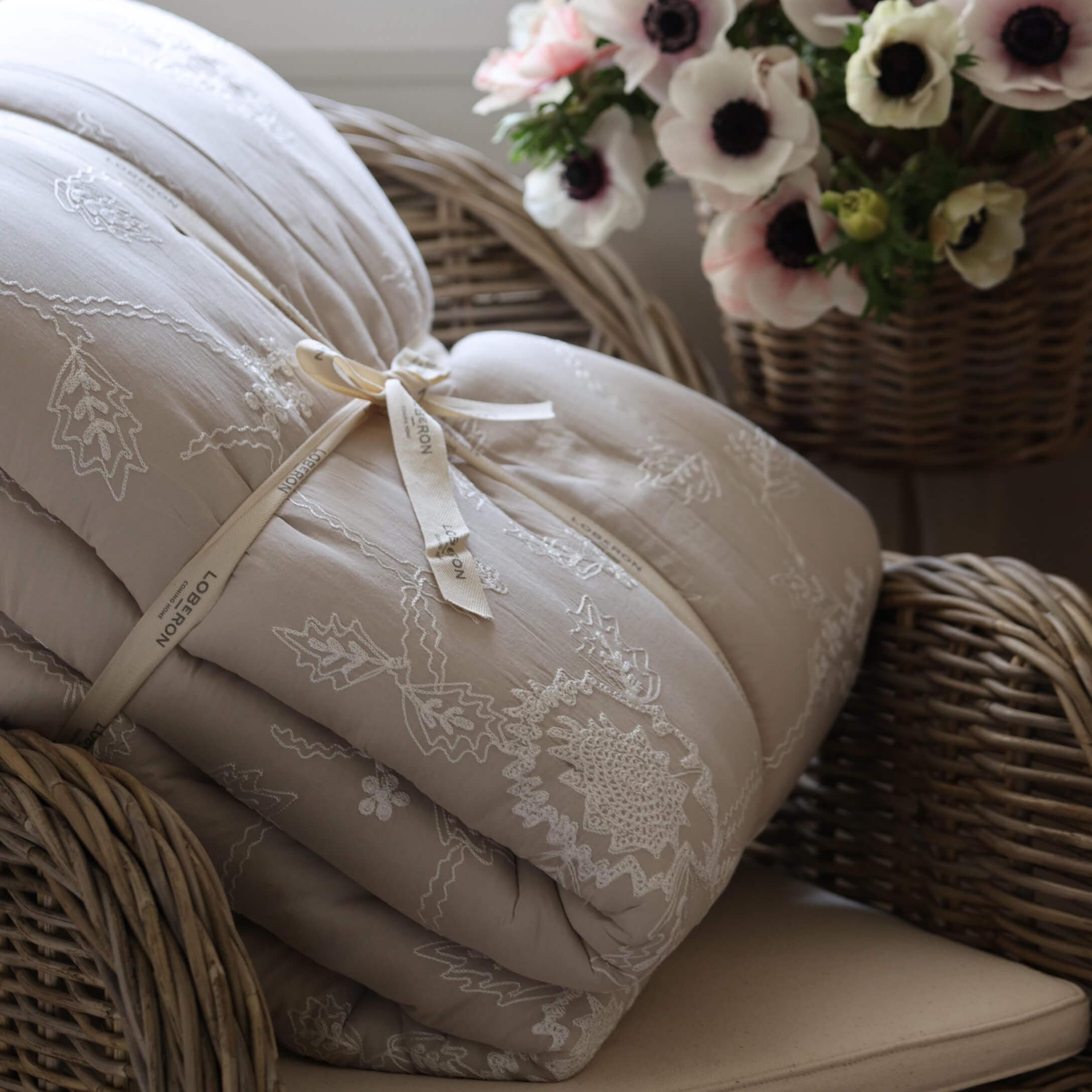 Beige gesteppte Tagesdecke mit Stickerei auf Korbsessel neben Blumenkorb, gemütliche Wohnraumdeko