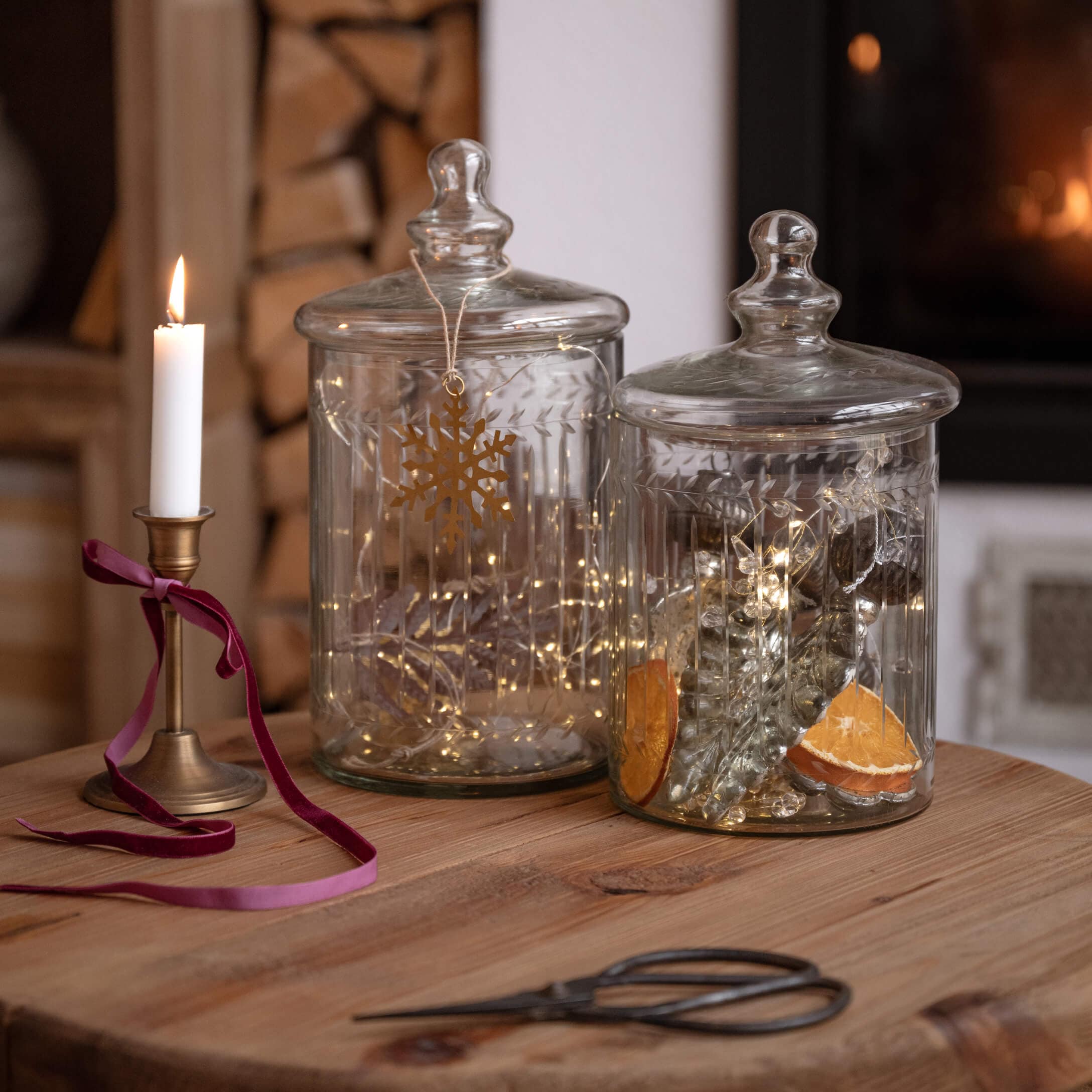 Transparente Glasbehälter mit Deckeln auf Holztisch, dekoriert mit Lichterketten und Kerze