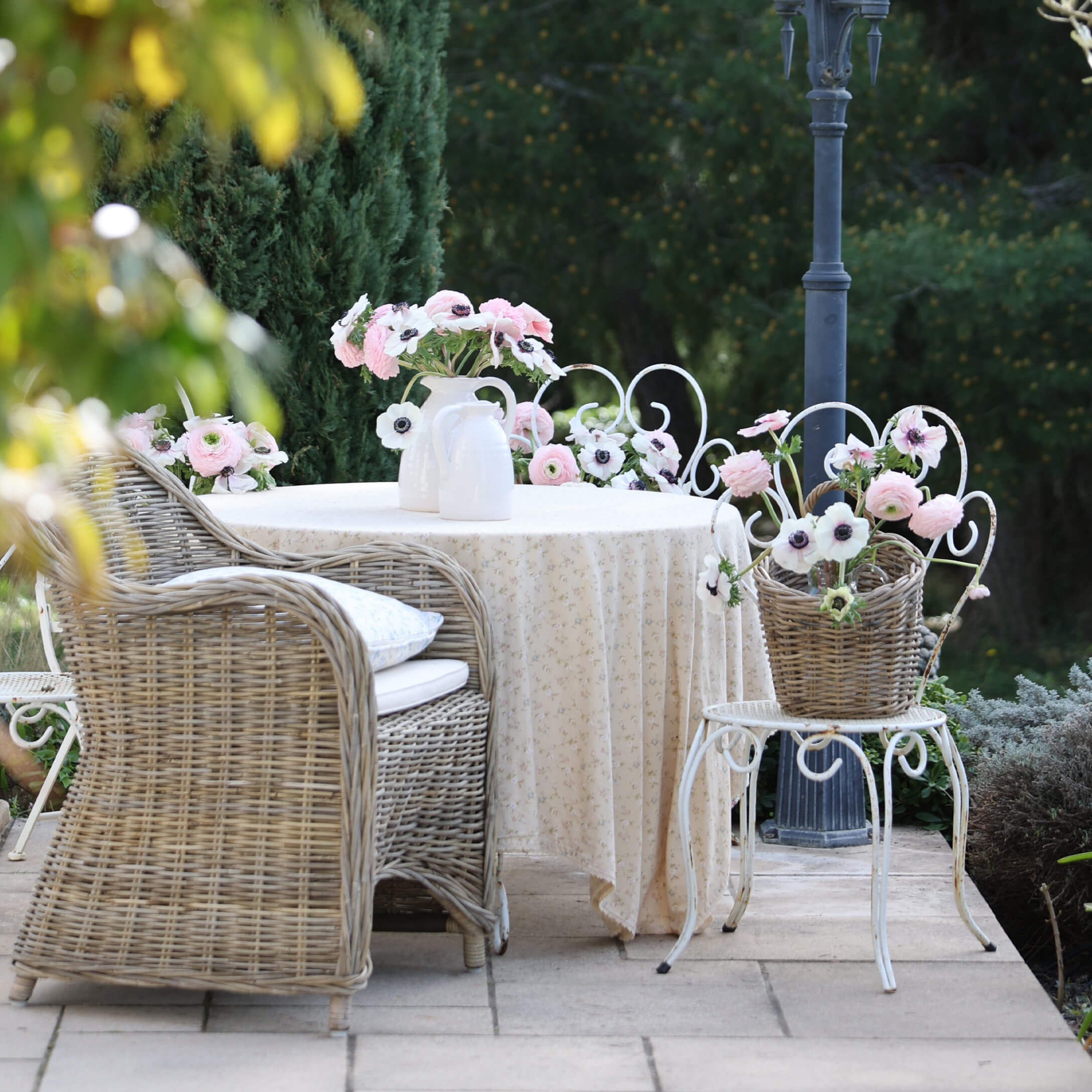 Garten mit Korbsessel, weissem Tisch mit Tischdecke und Blumen in Vasen, romantische Dekoration