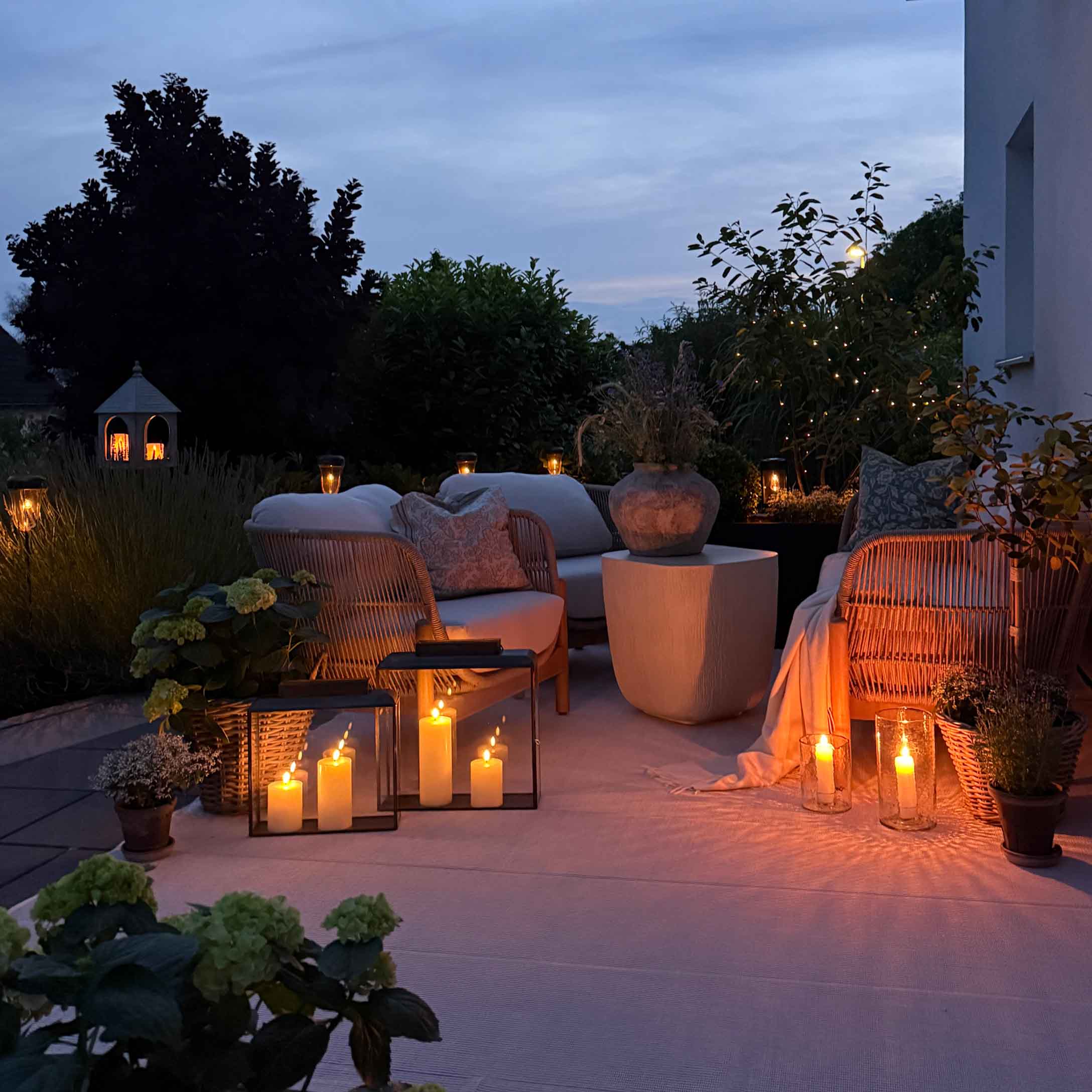 Gemütlicher Garten mit weissen Kissen auf Möbeln und dekorativen Kerzen am Abend