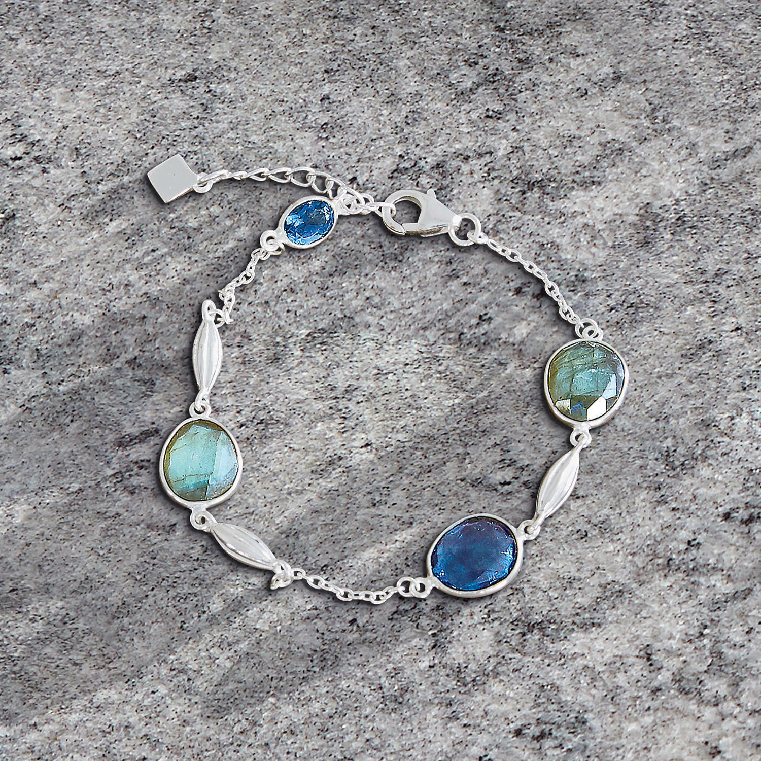 Feines Silberarmband mit blauen und grünen Steinen auf grauem Hintergrund