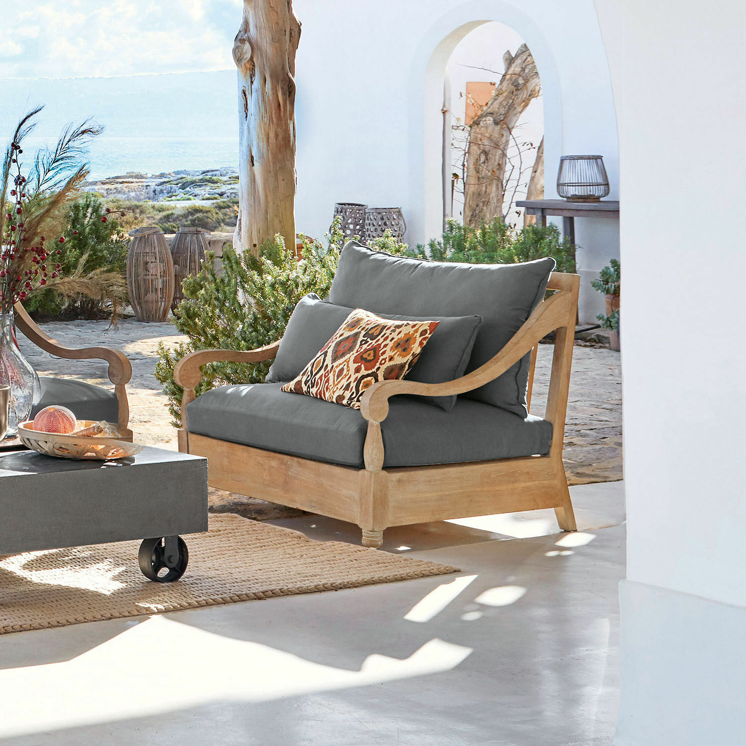 Sessel Montcassin Gartensofa aus Holz mit grauen Polstern und dekorativem Kissen in warmen Farben.