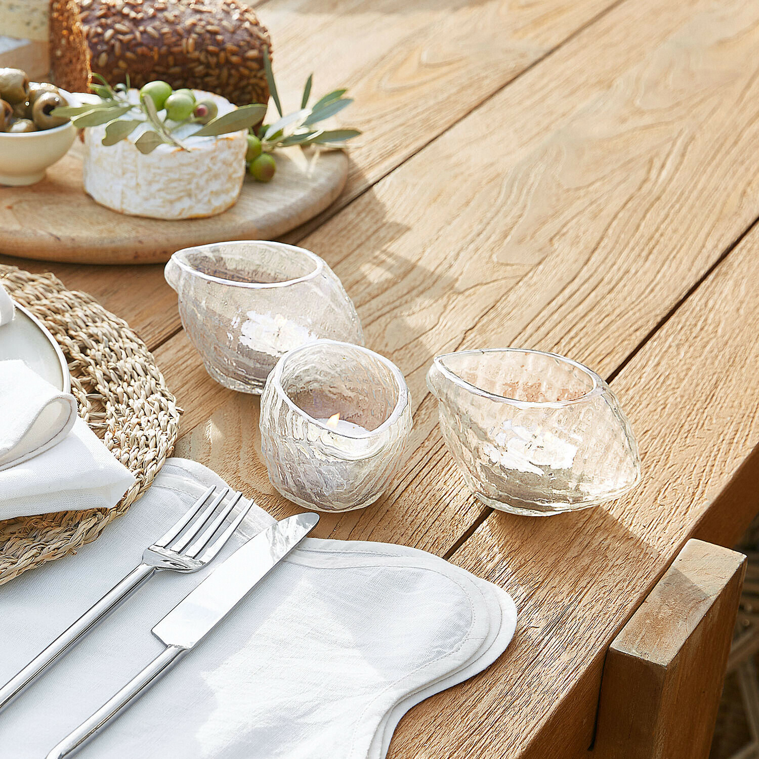 Teelichthalter 3er Set Wynska Drei transparente Glas-Teelichthalter mit unregelmäßiger Form auf Holztisch neben Besteck