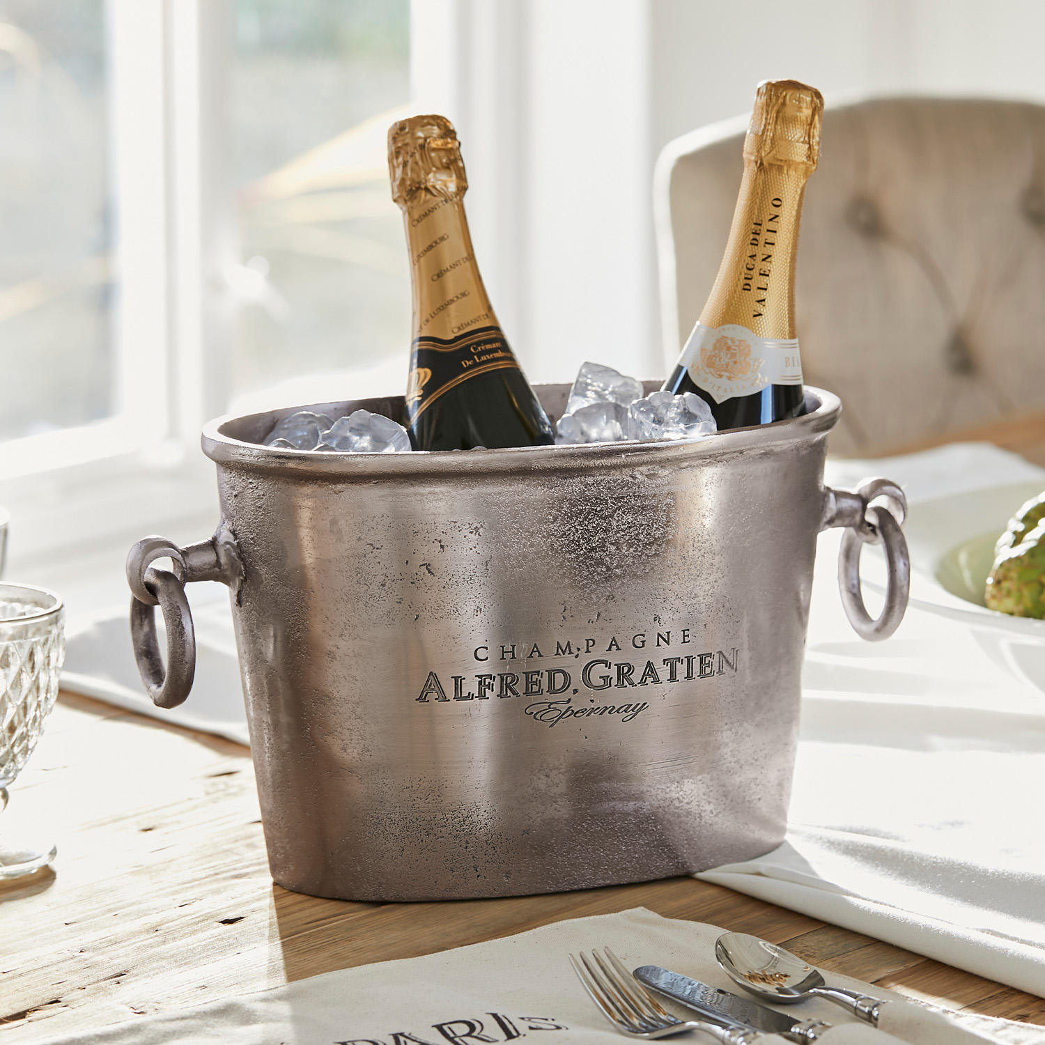 Metall Champagnerkühler mit zwei Flaschen und Eis auf Holztisch in hellem Raum